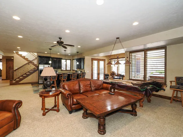 Spacious recreation room featuring carpet flooring, recessed lighting, a ceiling fan, and a built-in wet bar with dark cabinetry