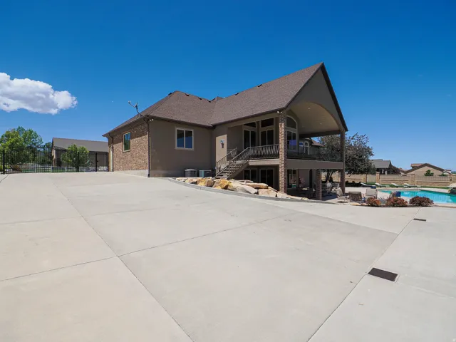 Spacious concrete driveway leading to a multi-level residence featuring a stucco and brick exterior, covered upper and lower patios, and an outdoor swimming pool