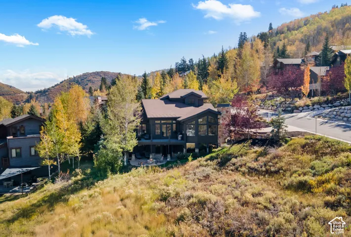 Multi-level custom residence featuring dark wood siding, a metal roof, expansive floor-to-ceiling windows, and a stone-clad exterior chimney