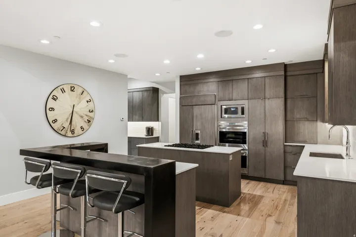 Kitchen with recessed lighting, light wood-style floors, built in appliances, dark stone countertops, and a breakfast bar