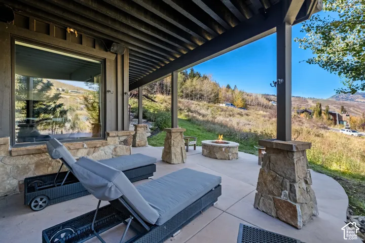 Covered patio featuring concrete flooring, stone-veneer column bases, and a built-in stone fire pit