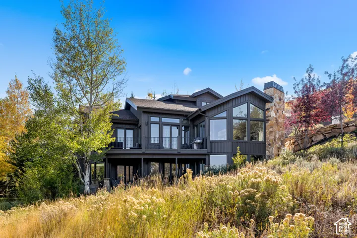 Multi-story mountain residence featuring dark-toned board and batten siding, extensive floor-to-ceiling windows, a stacked stone chimney, and an elevated deck with metal railings
