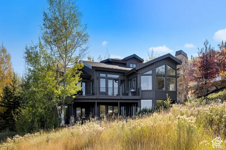 Multi-level exterior featuring dark vertical siding, large floor-to-ceiling windows, stone chimney masonry, and a raised wooden deck with metal railing