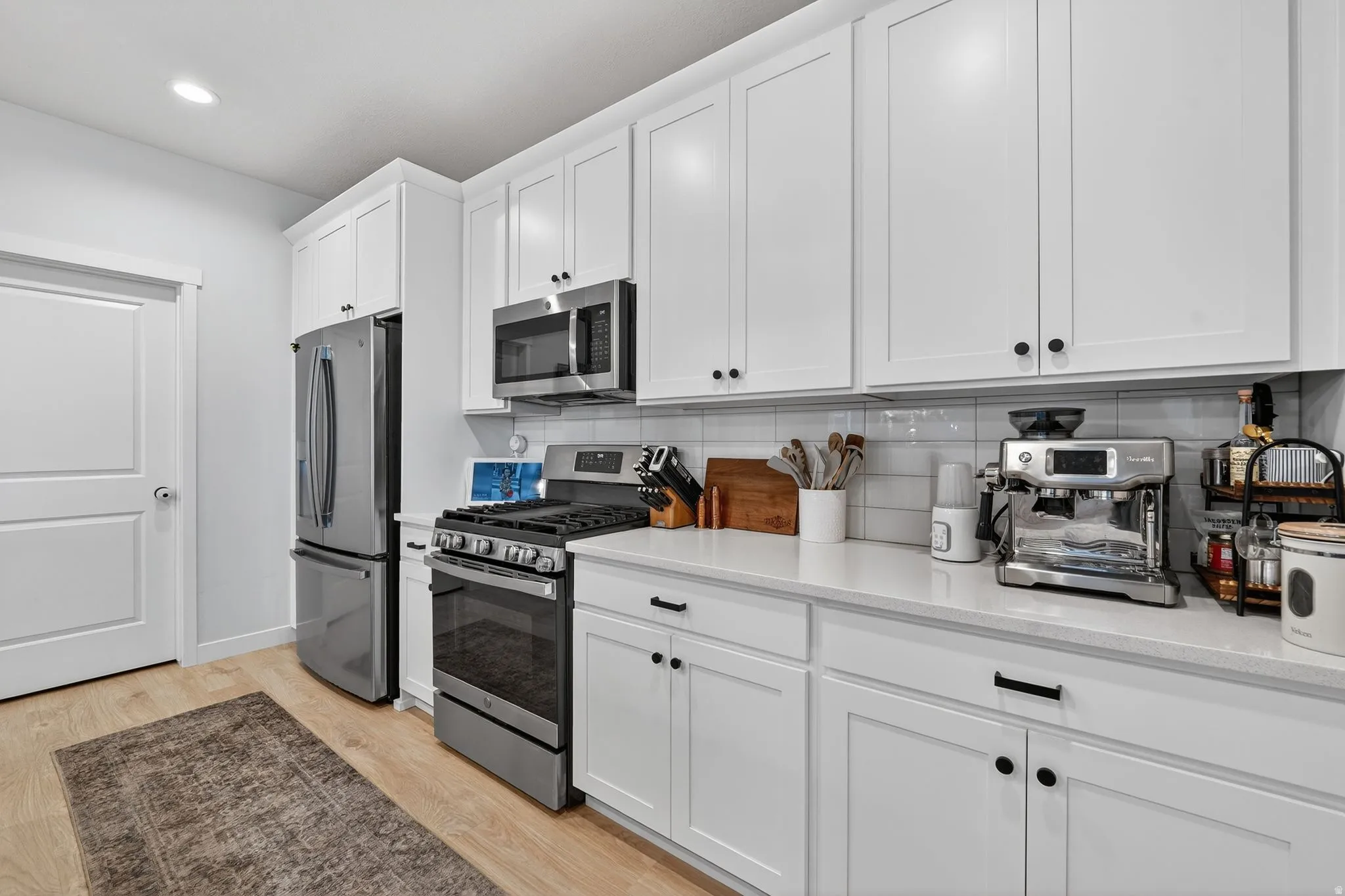 Kitchen featuring stainless steel appliances, white cabinetry, light wood-style flooring, light stone countertops, and tasteful backsplash