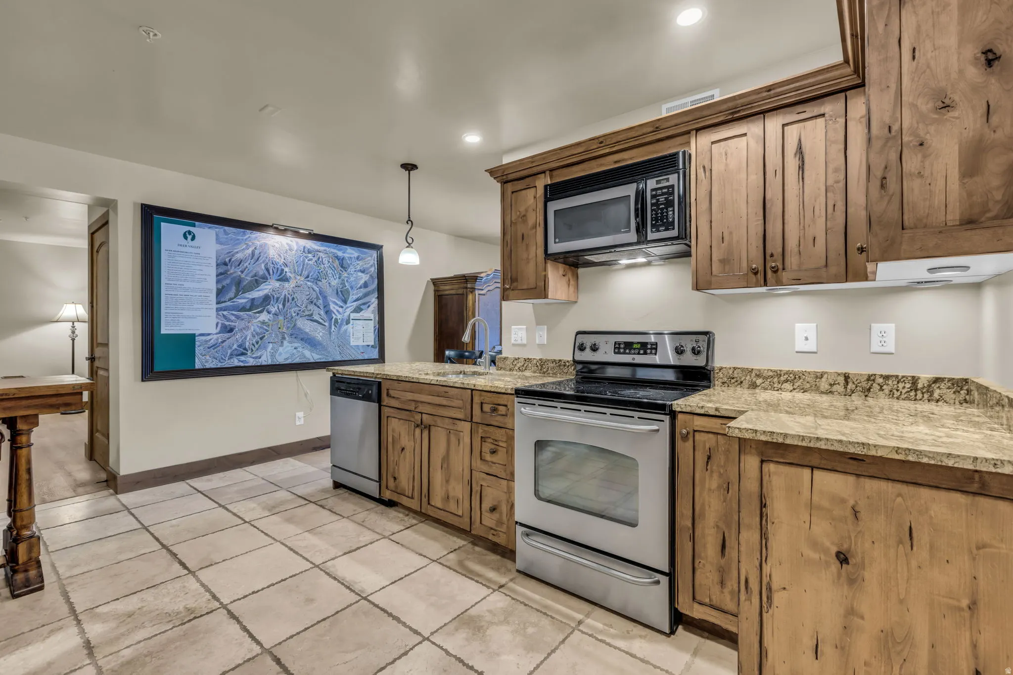 Kitchen featuring stainless steel appliances, wood finish cabinetry, decorative light fixtures, and light stone countertops