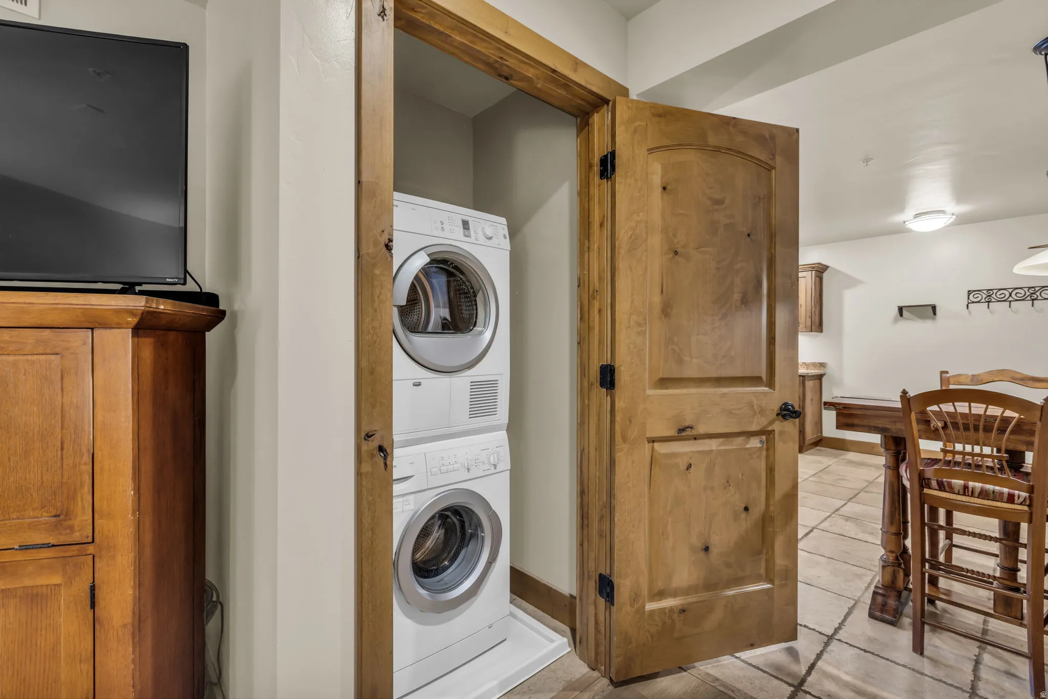 Laundry area with stacked washer and clothes dryer and light tile patterned flooring