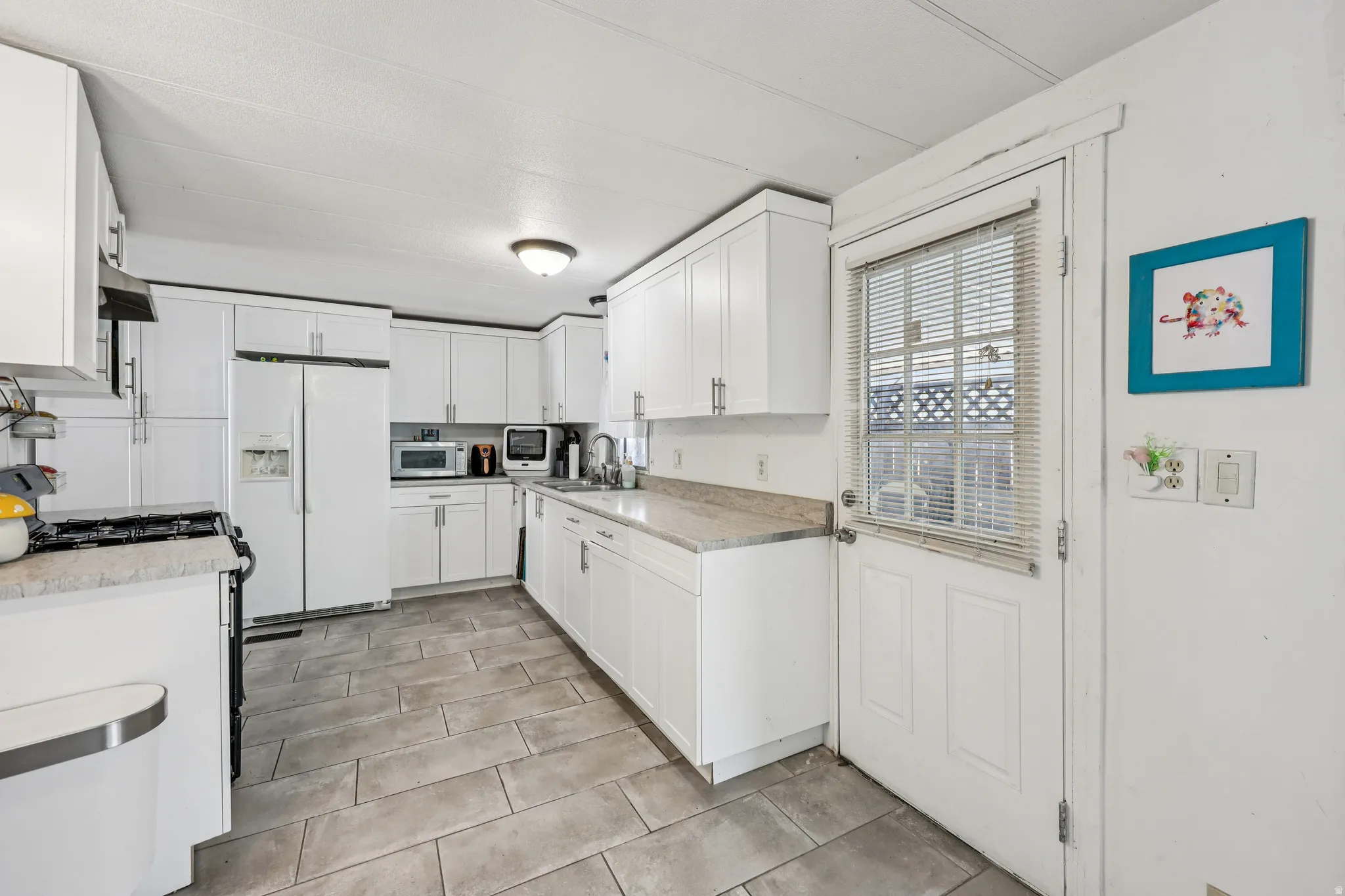 Kitchen with white cabinetry, white refrigerator with ice dispenser, stainless steel gas range, light stone counters, and ventilation hood