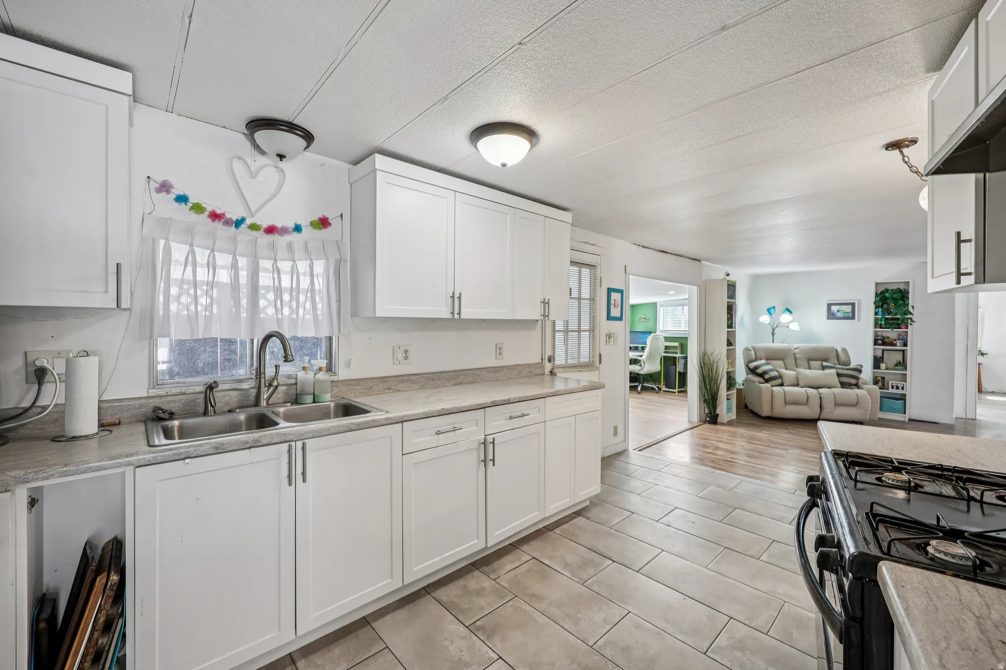 Kitchen featuring black range with gas cooktop, open floor plan, white cabinets, light countertops, and a textured ceiling