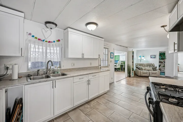 Kitchen featuring black range with gas cooktop, open floor plan, white cabinets, light countertops, and a textured ceiling