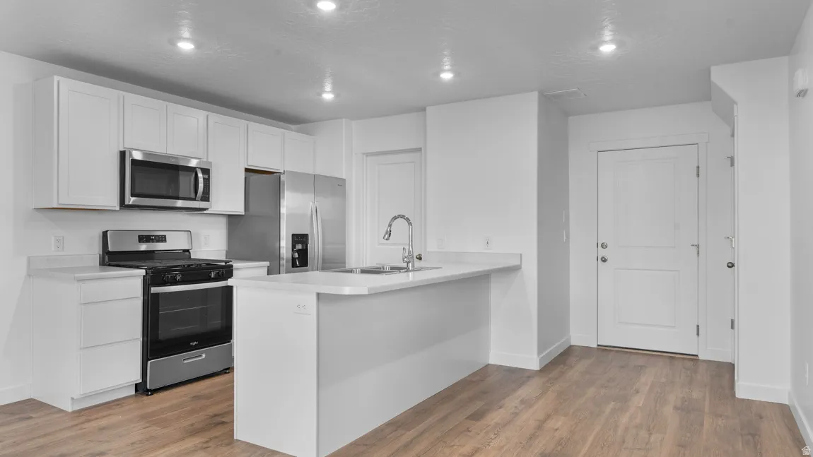 Kitchen with stainless steel appliances, light countertops, white cabinetry, dark wood-style floors, and recessed lighting