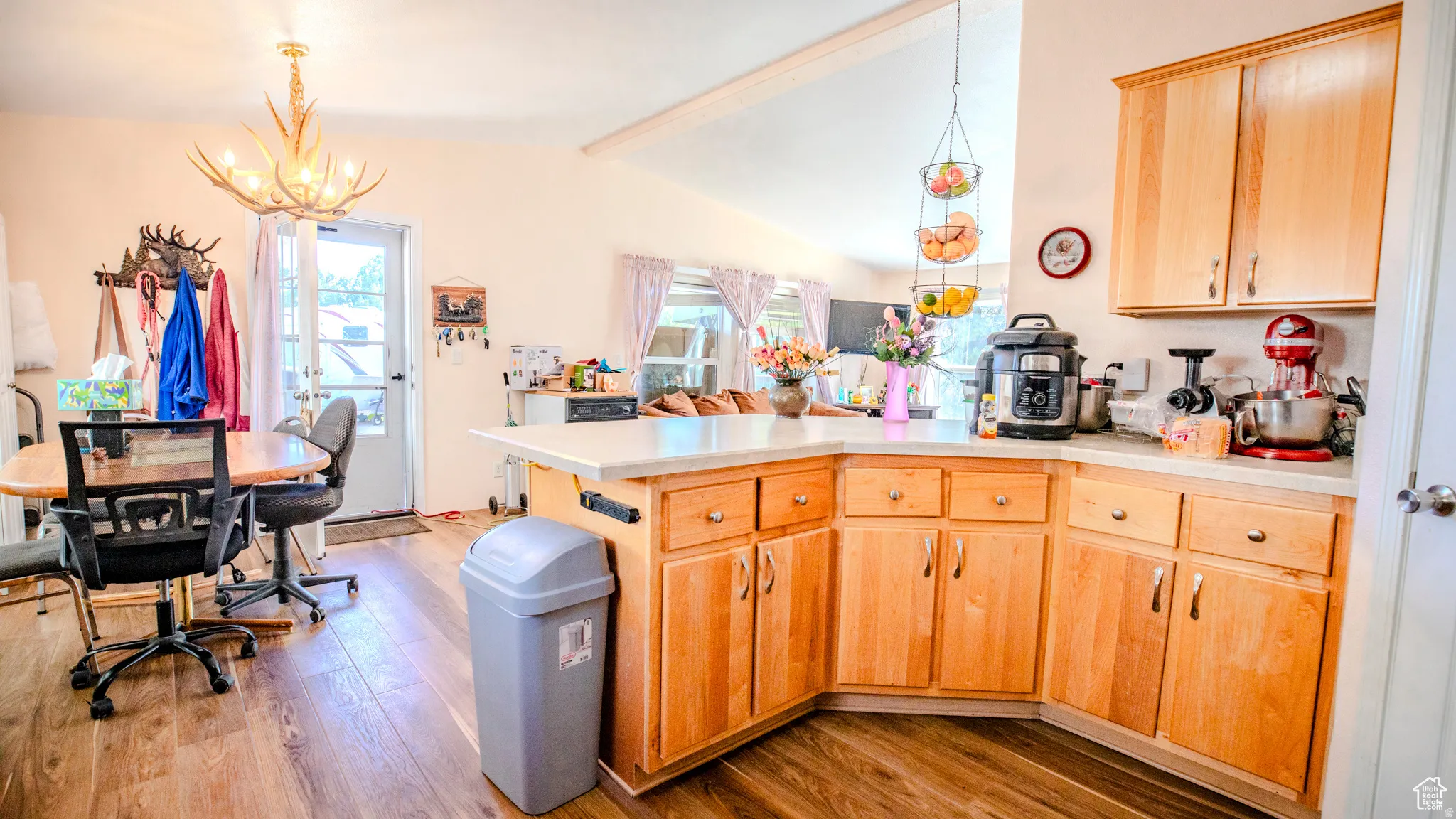 Kitchen featuring a peninsula, vaulted ceiling with beams, light wood finish cabinets, light wood-type flooring, and a chandelier