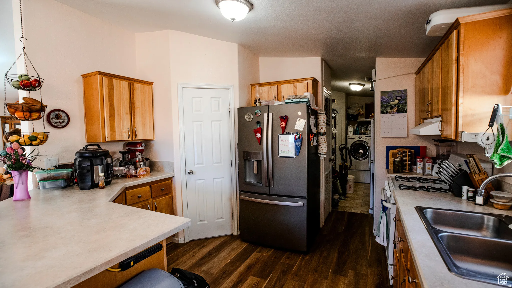 Kitchen featuring light countertops, stainless steel fridge with ice dispenser, wood finish cabinetry, dark wood-style flooring, and a peninsula