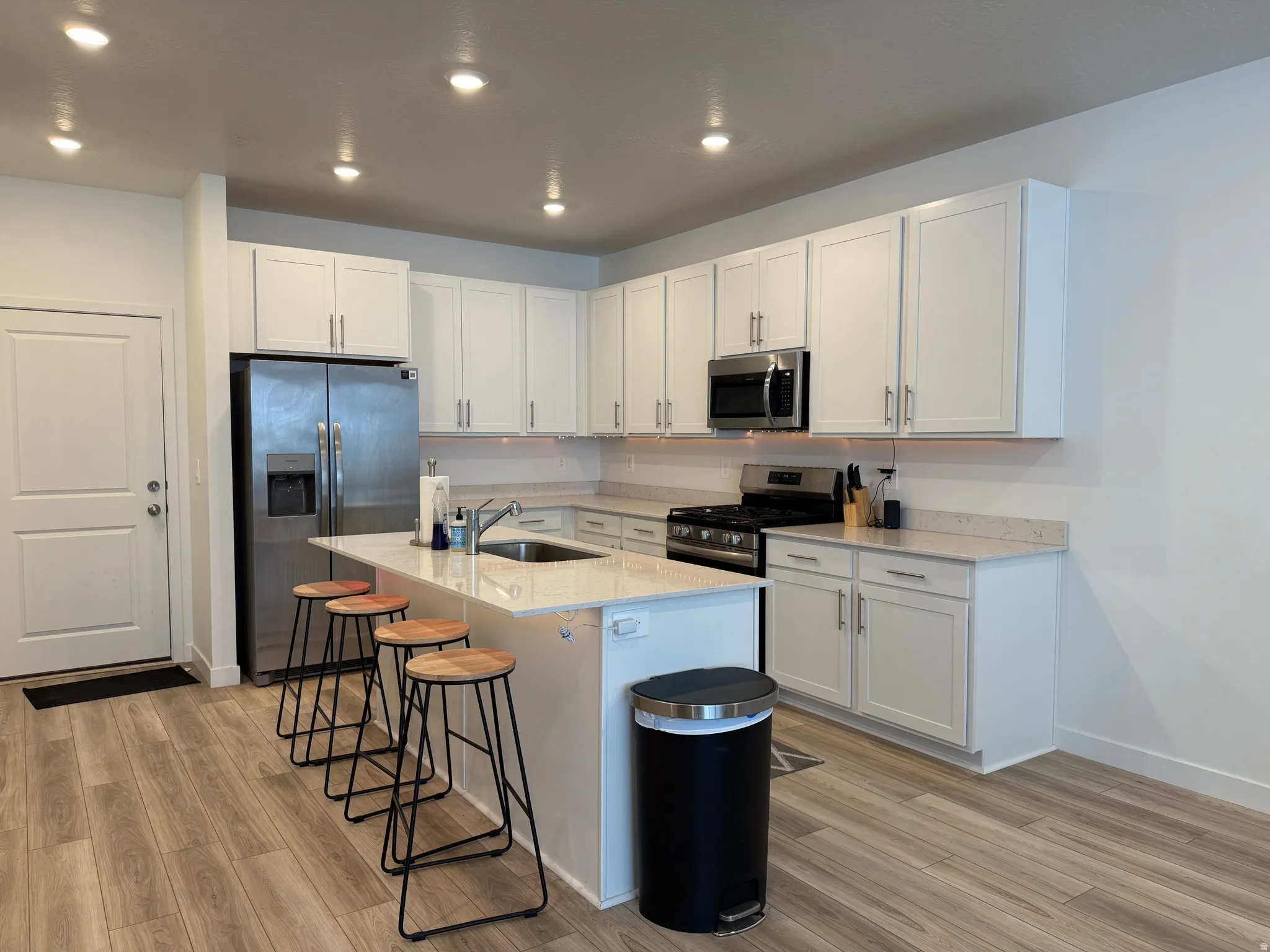 Kitchen featuring stainless steel appliances, white cabinets, light stone countertops, an island with sink, and recessed lighting
