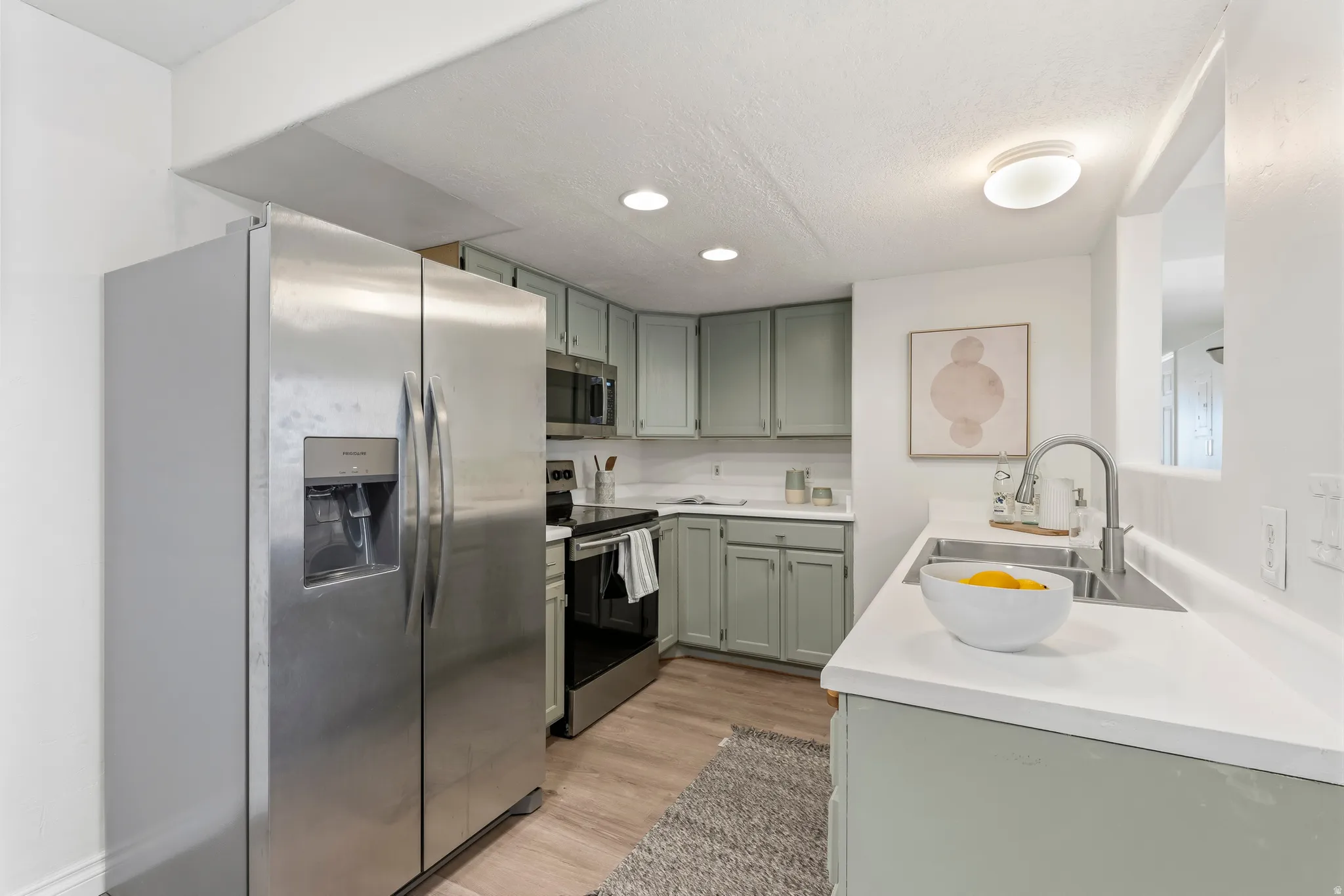 Kitchen featuring stainless steel appliances, light countertops, light wood-style floors, green cabinets, and recessed lighting