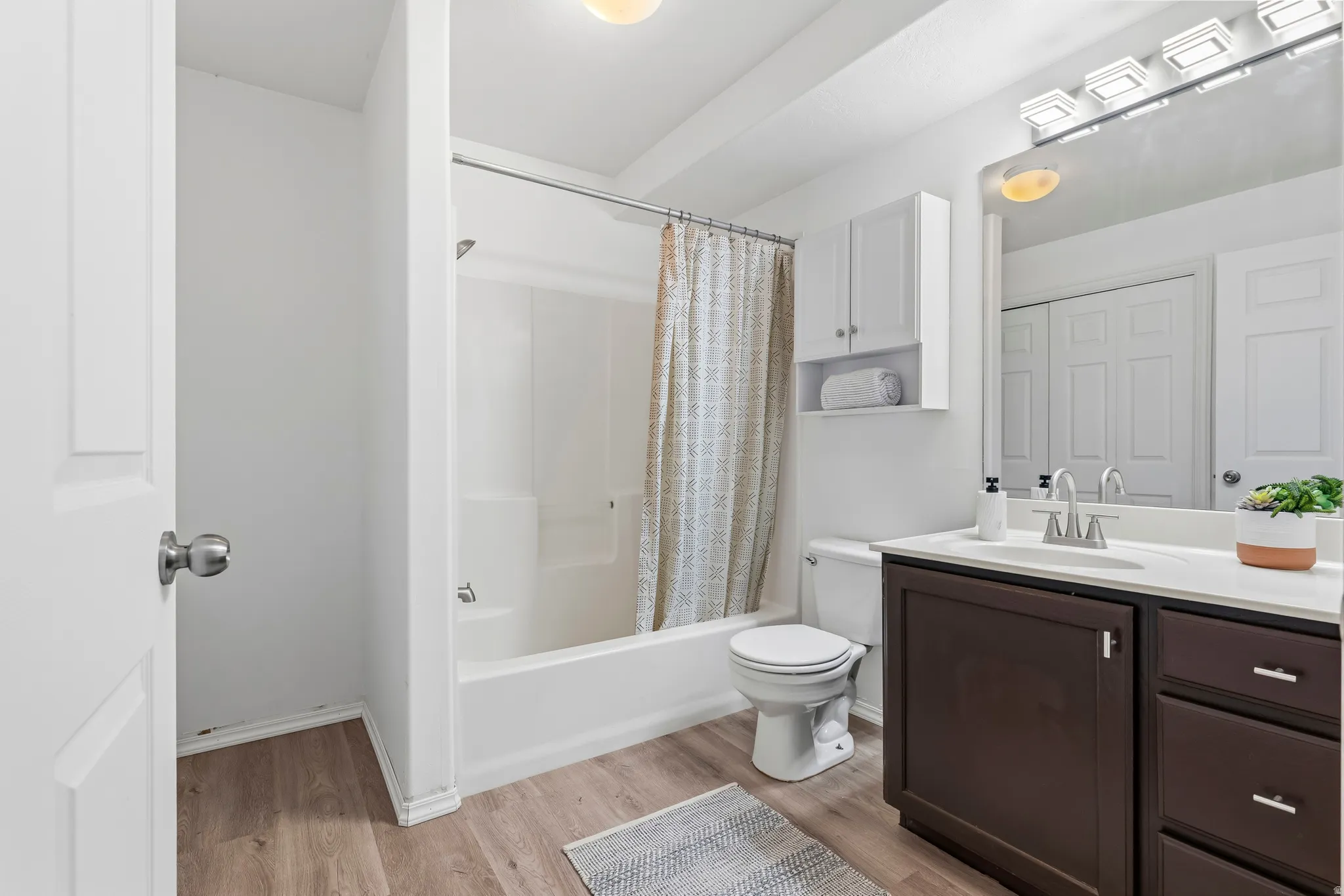 Full bathroom with vanity, light wood-style flooring, shower / bathtub combination with curtain, and a closet