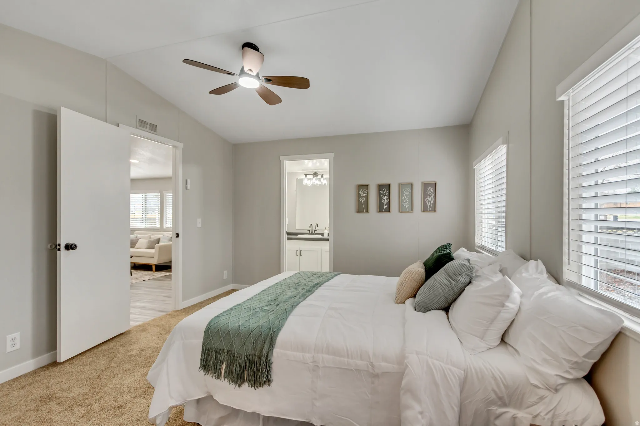 Bedroom with vaulted ceiling, carpet floors, multiple windows, a ceiling fan, and ensuite bath