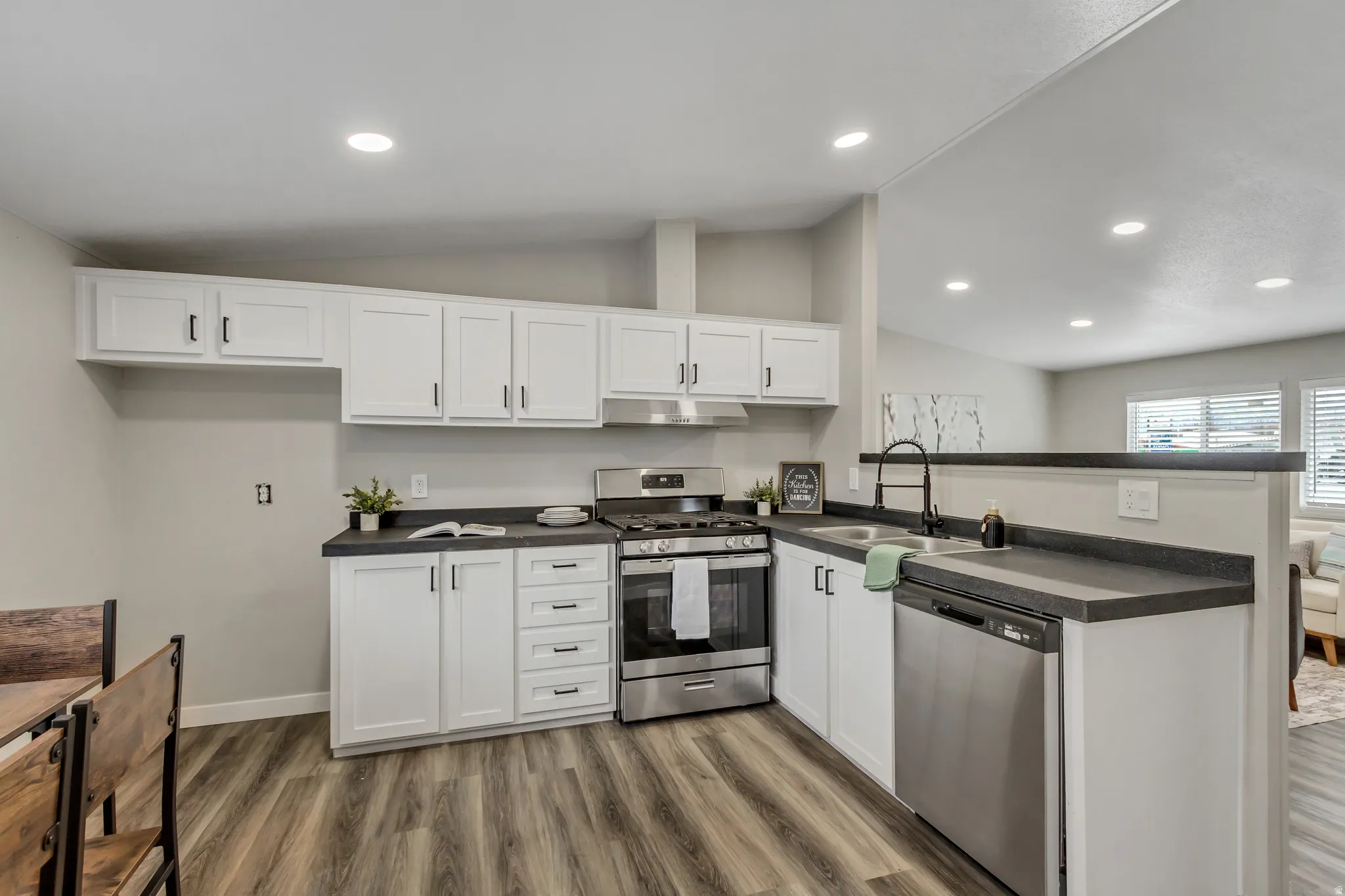 Kitchen with dark countertops, stainless steel appliances, white cabinetry, a peninsula, and lofted ceiling