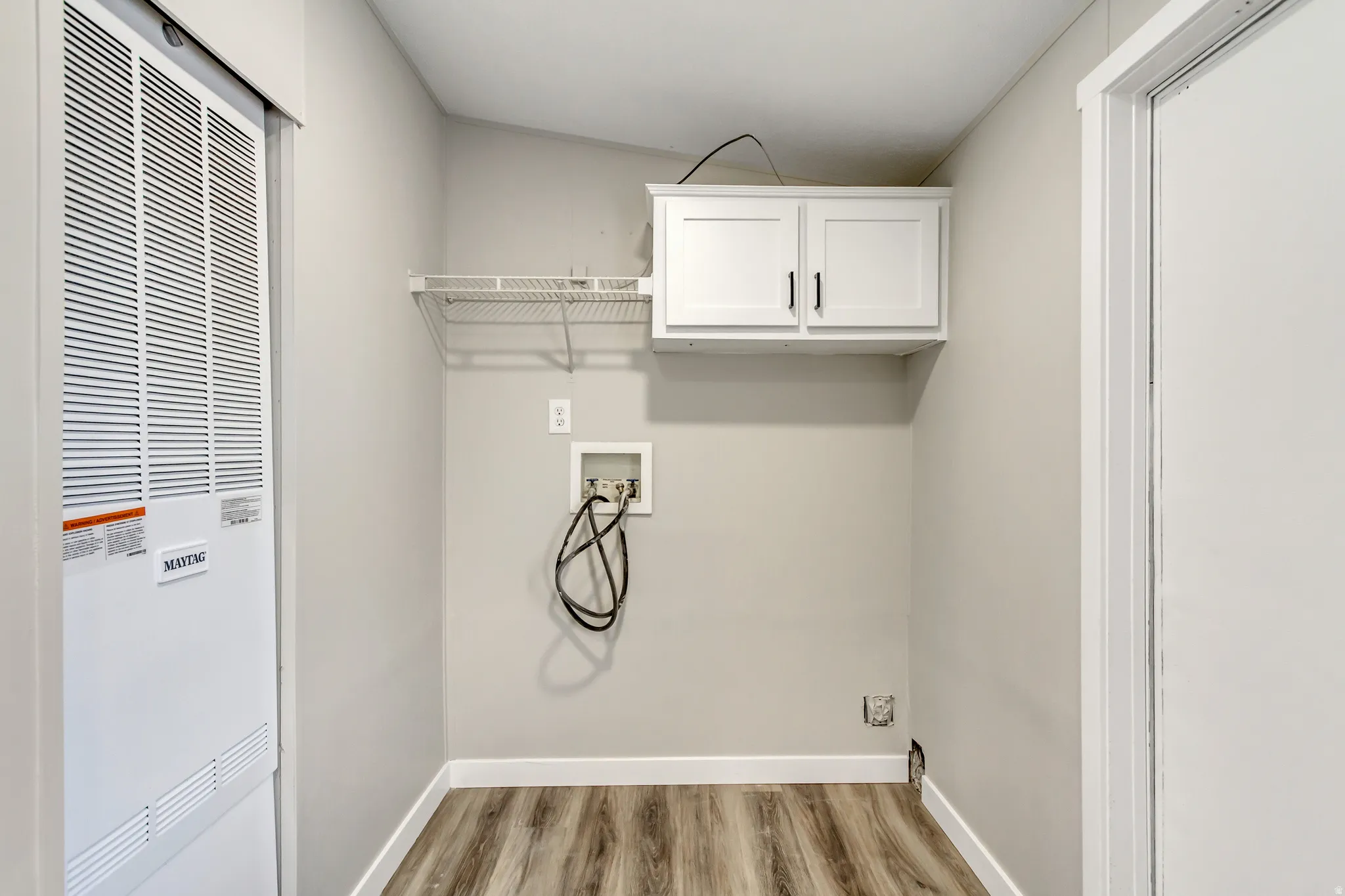Laundry area featuring a heating unit, hookup for a washing machine, light wood-style flooring, and cabinet space