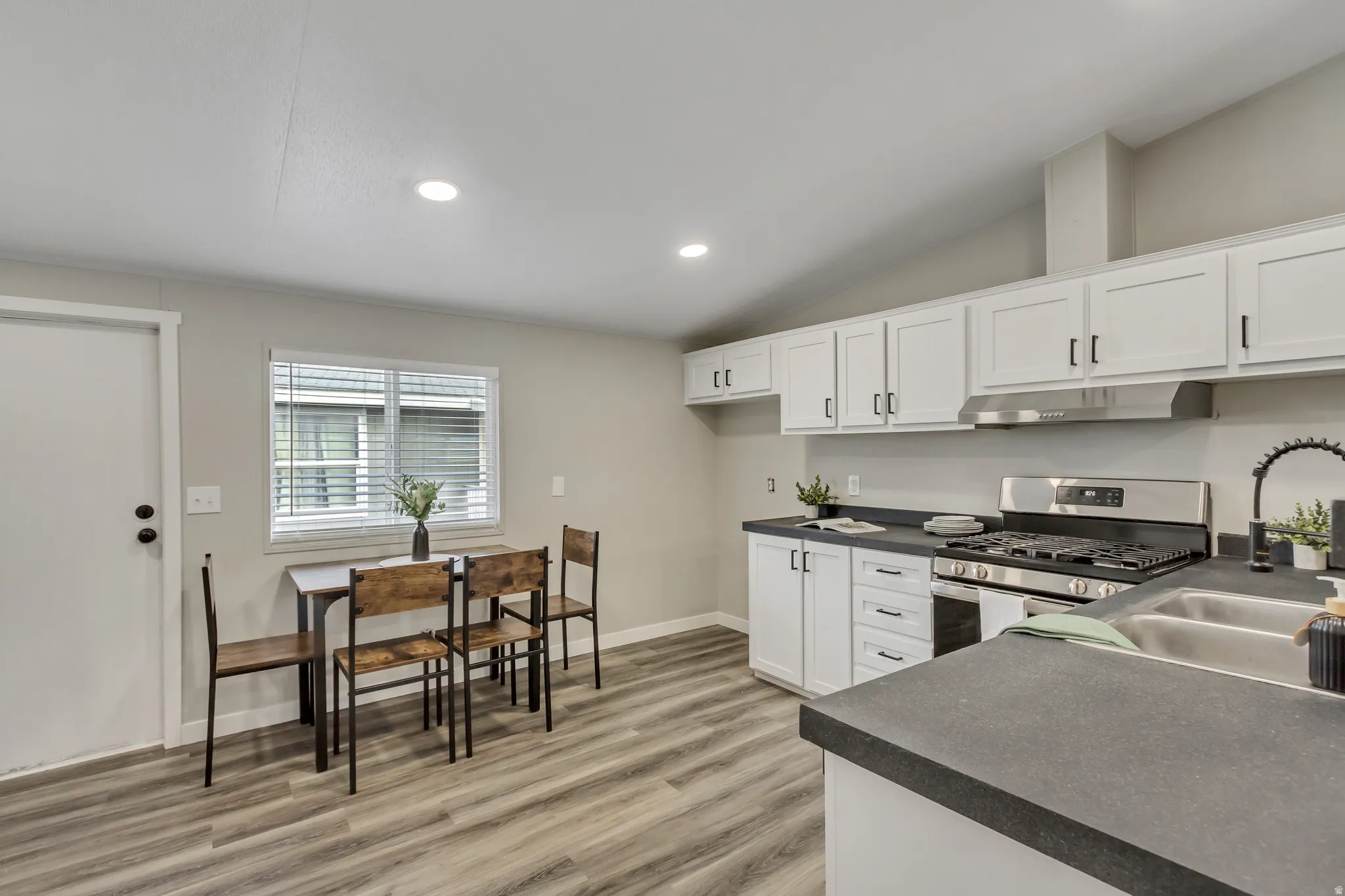 Kitchen featuring dark countertops, white cabinetry, vaulted ceiling, stainless steel gas range, and light wood-style floors