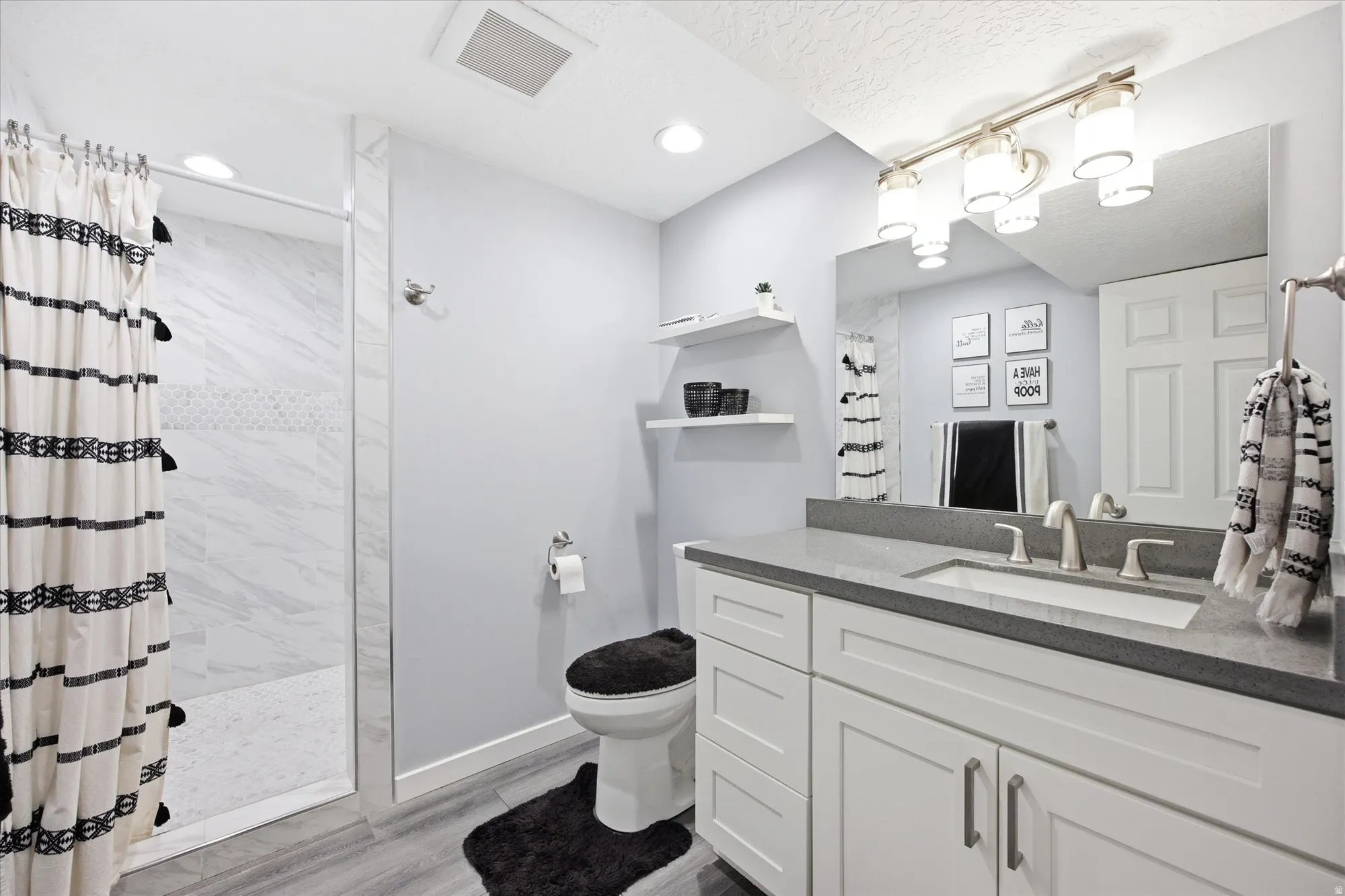 Full bath featuring vanity, a marble finish shower, and light wood finished floors