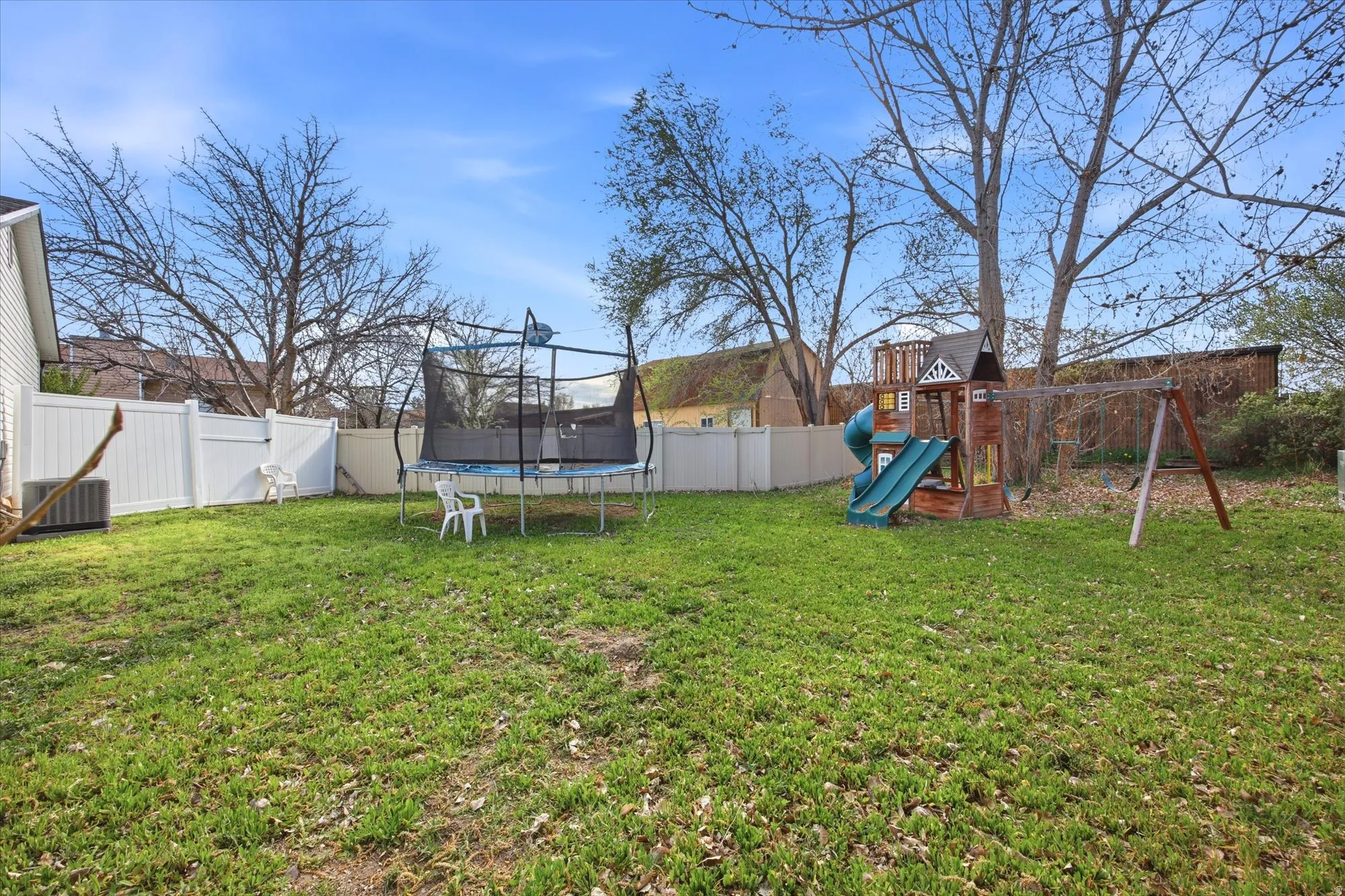 Fenced backyard featuring a trampoline and a playground