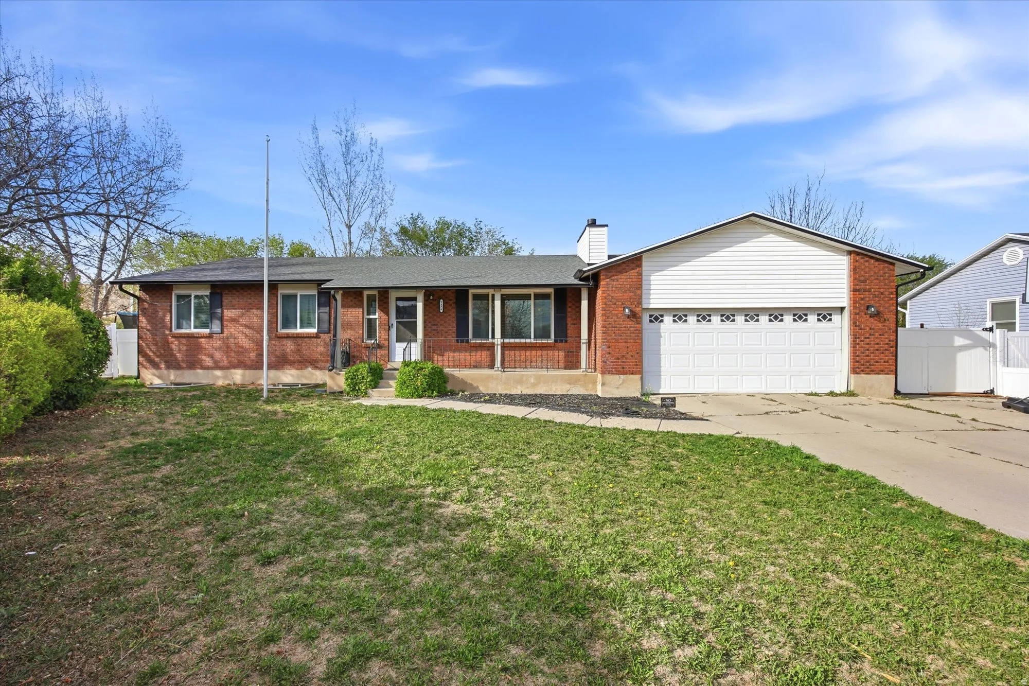 Ranch-style home with brick siding, a garage, concrete driveway, a chimney, and a porch