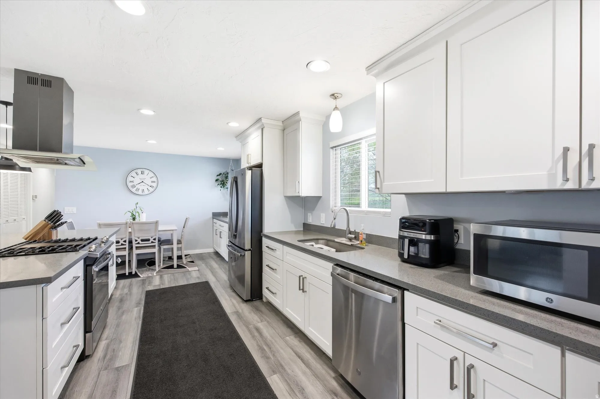 Kitchen featuring stainless steel appliances, island range hood, white cabinetry, light wood-type flooring, and recessed lighting