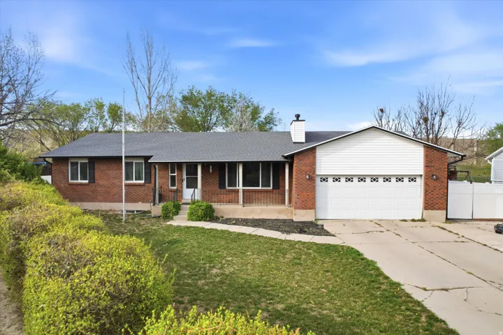 Single story home with covered porch, brick siding, driveway, an attached garage, and a chimney