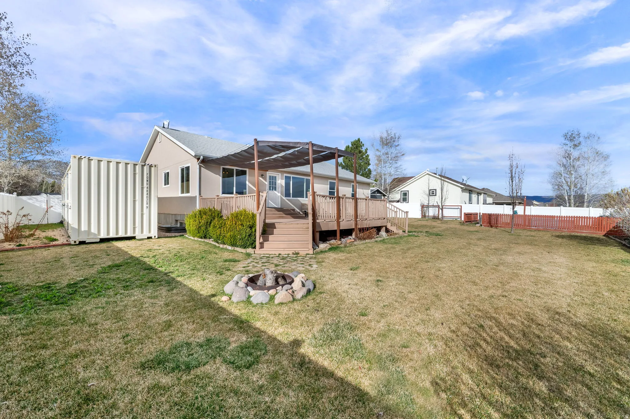 Back of house with a fenced backyard, a deck, and an outdoor fire pit