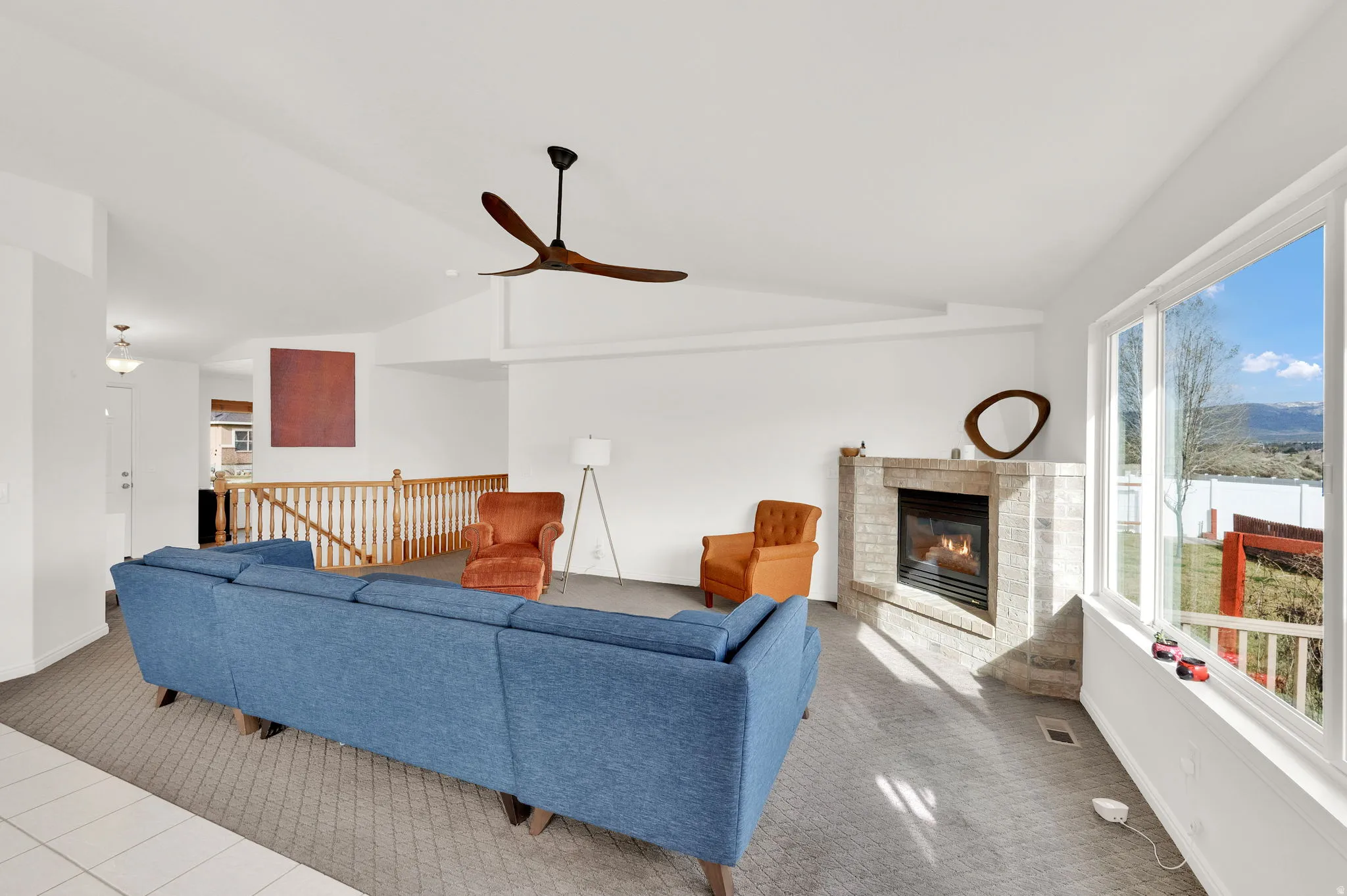 Carpeted living area featuring vaulted ceiling, a fireplace, and a ceiling fan