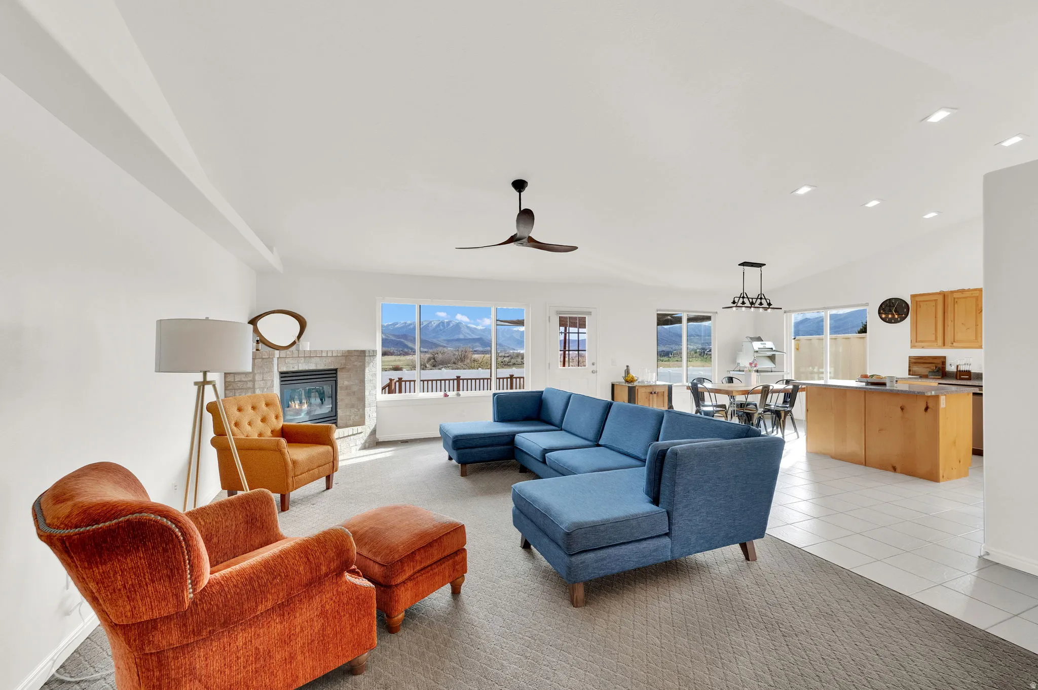 Great room with open kitchen and island, a mountain view, a brick fireplace, a ceiling fan and vaulted ceiling.