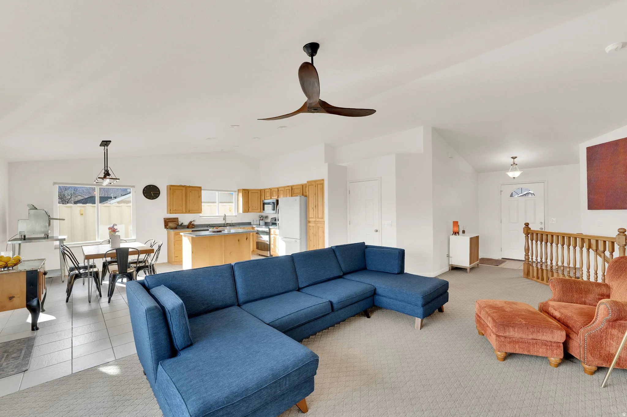 Living area with lofted ceiling, ceiling fan, and light carpet with view of the entry way.