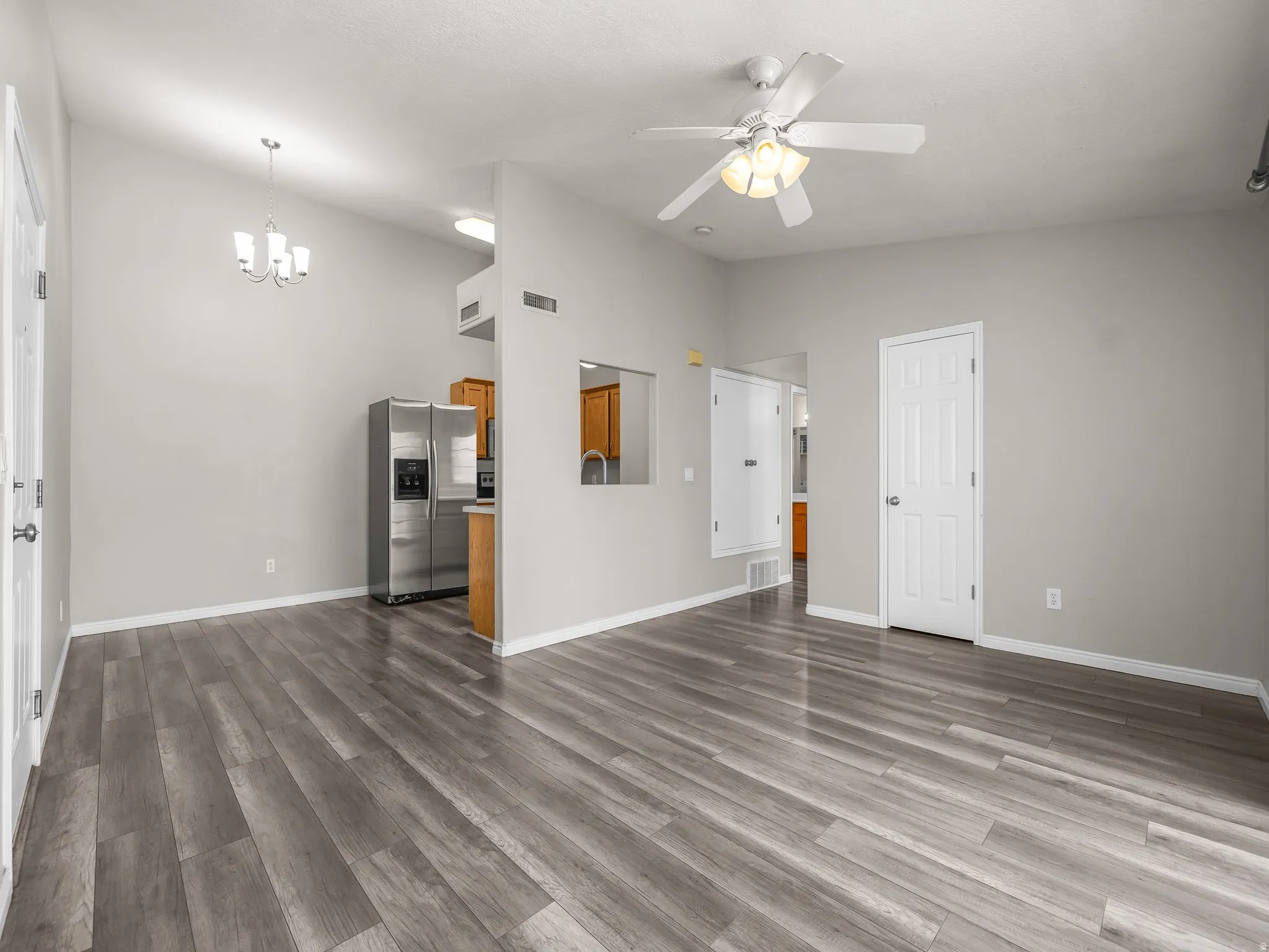 Unfurnished living room featuring ceiling fan, light wood-type flooring, suspended lighting, and lofted ceiling