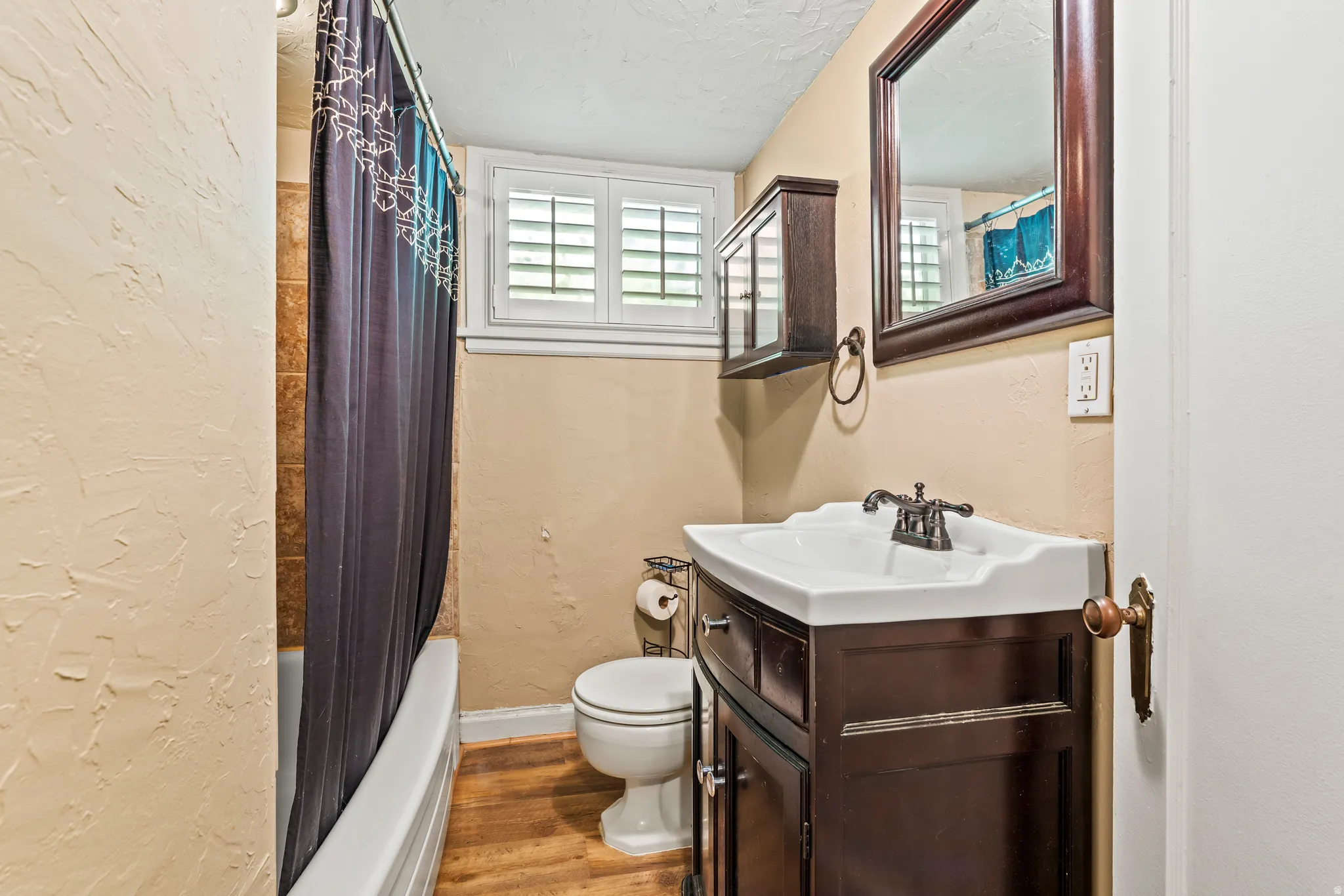 Bathroom with a textured wall, vanity, light wood-style floors, a textured ceiling, and shower / bath combination with curtain