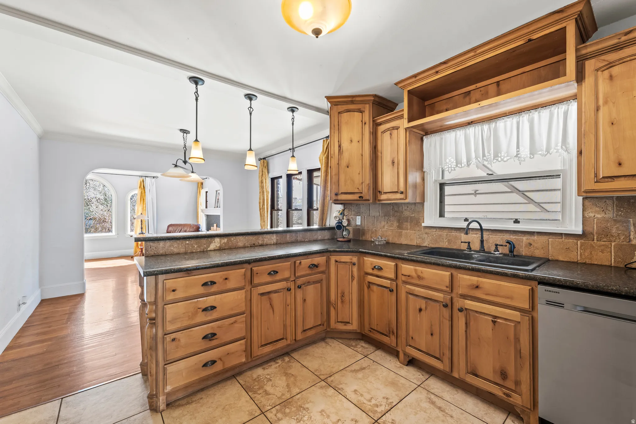 Kitchen with stainless steel dishwasher, a peninsula, backsplash, decorative light fixtures, and wood finish cabinetry