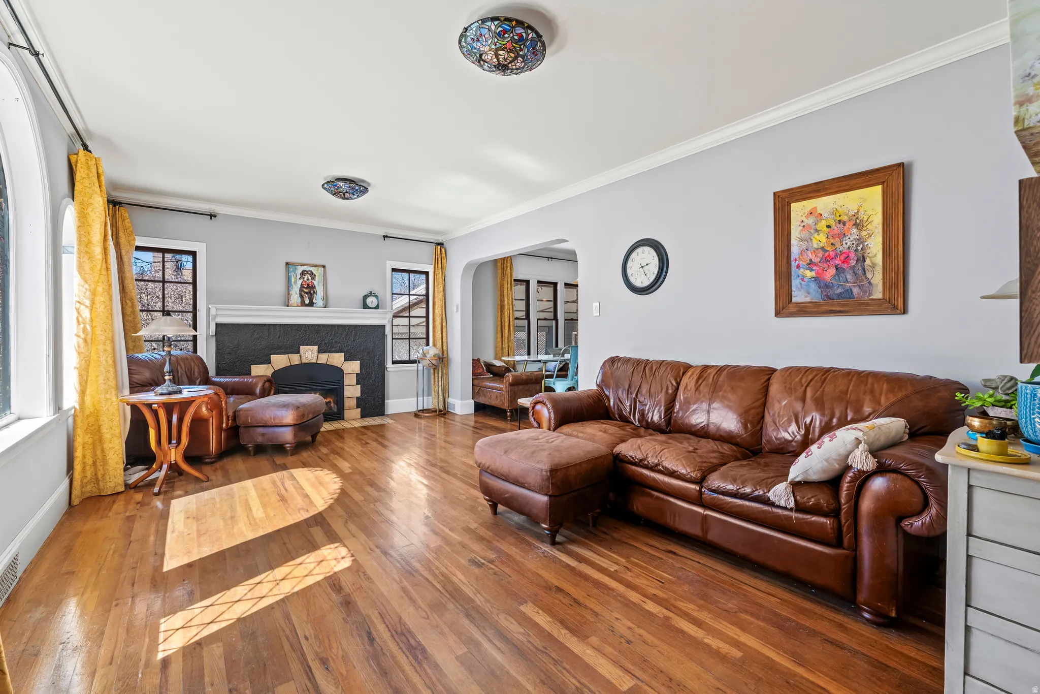 Living area featuring arched walkways, hardwood / wood-style floors, a fireplace with flush hearth, crown molding, and healthy amount of natural light