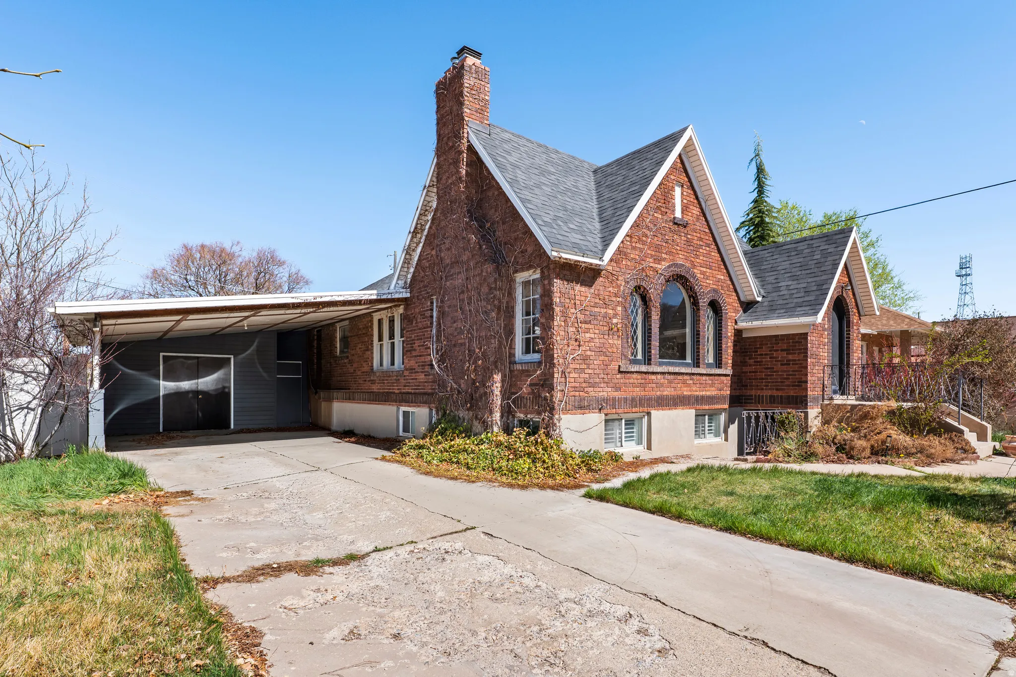 View of property exterior featuring brick siding, an attached carport, driveway, a lawn, and a chimney