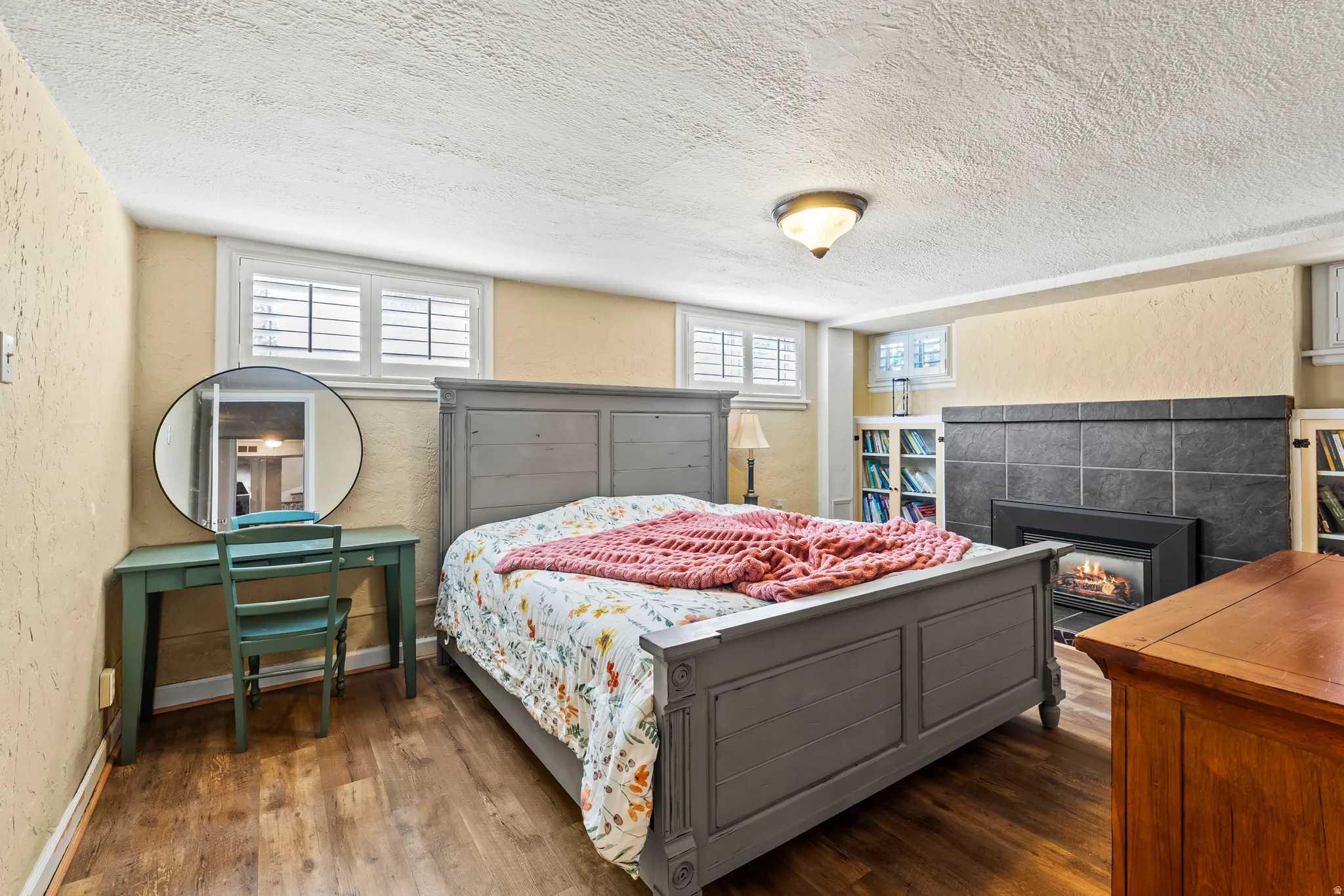 Bedroom with a textured wall, dark wood-style flooring, a textured ceiling, and a fireplace