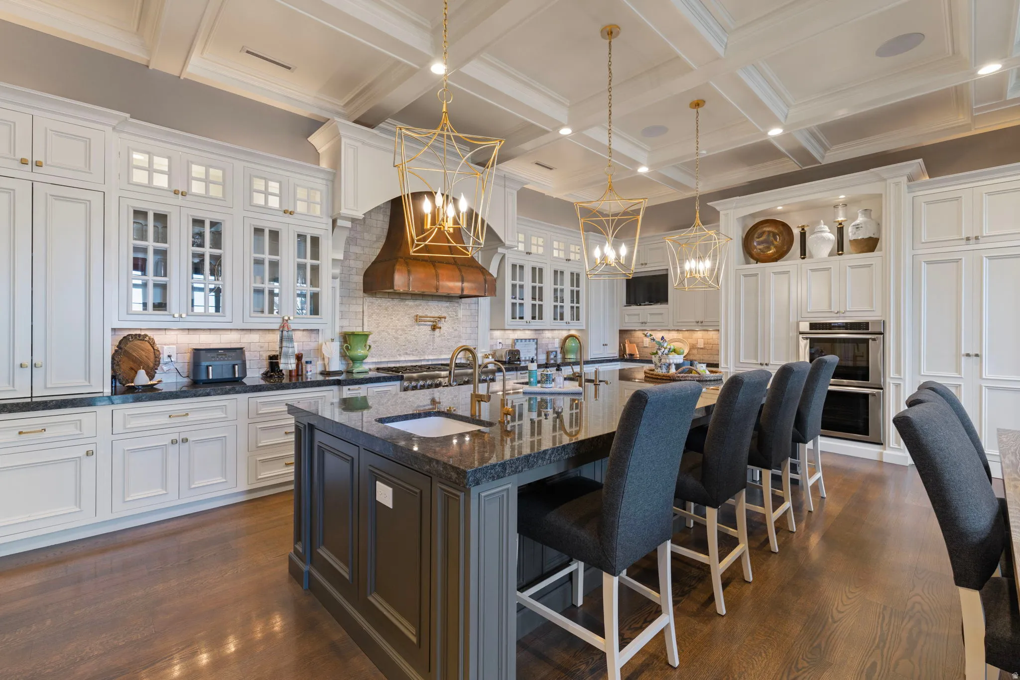 Kitchen with a center island with sink, dark stone counters, glass fronted cabinets, a kitchen bar, and double oven