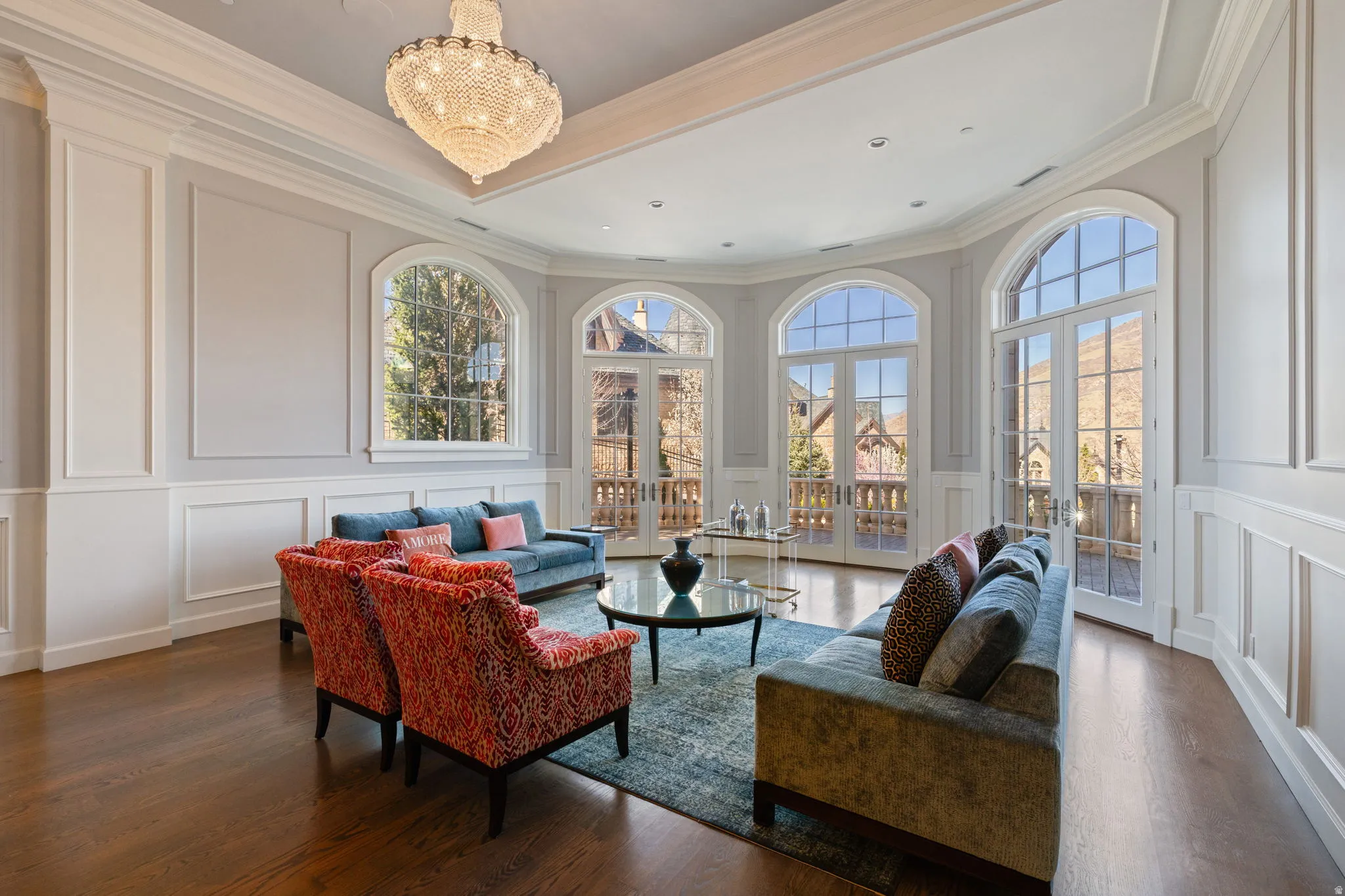 Living area with a decorative wall, french doors, suspended lighting, wood finished floors, and ornamental molding