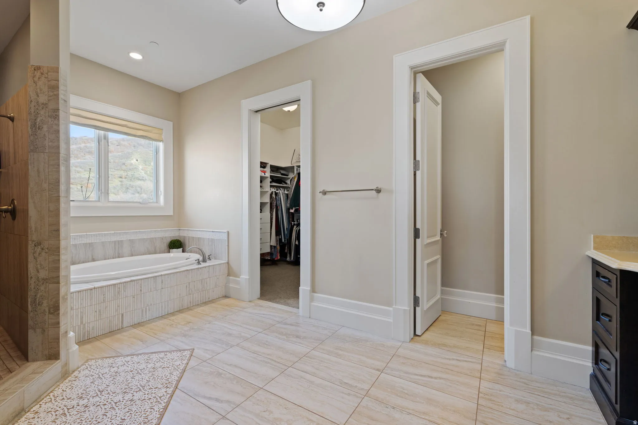 Full bath featuring a spacious closet, a bath, vanity, a tile shower, and light tile patterned floors