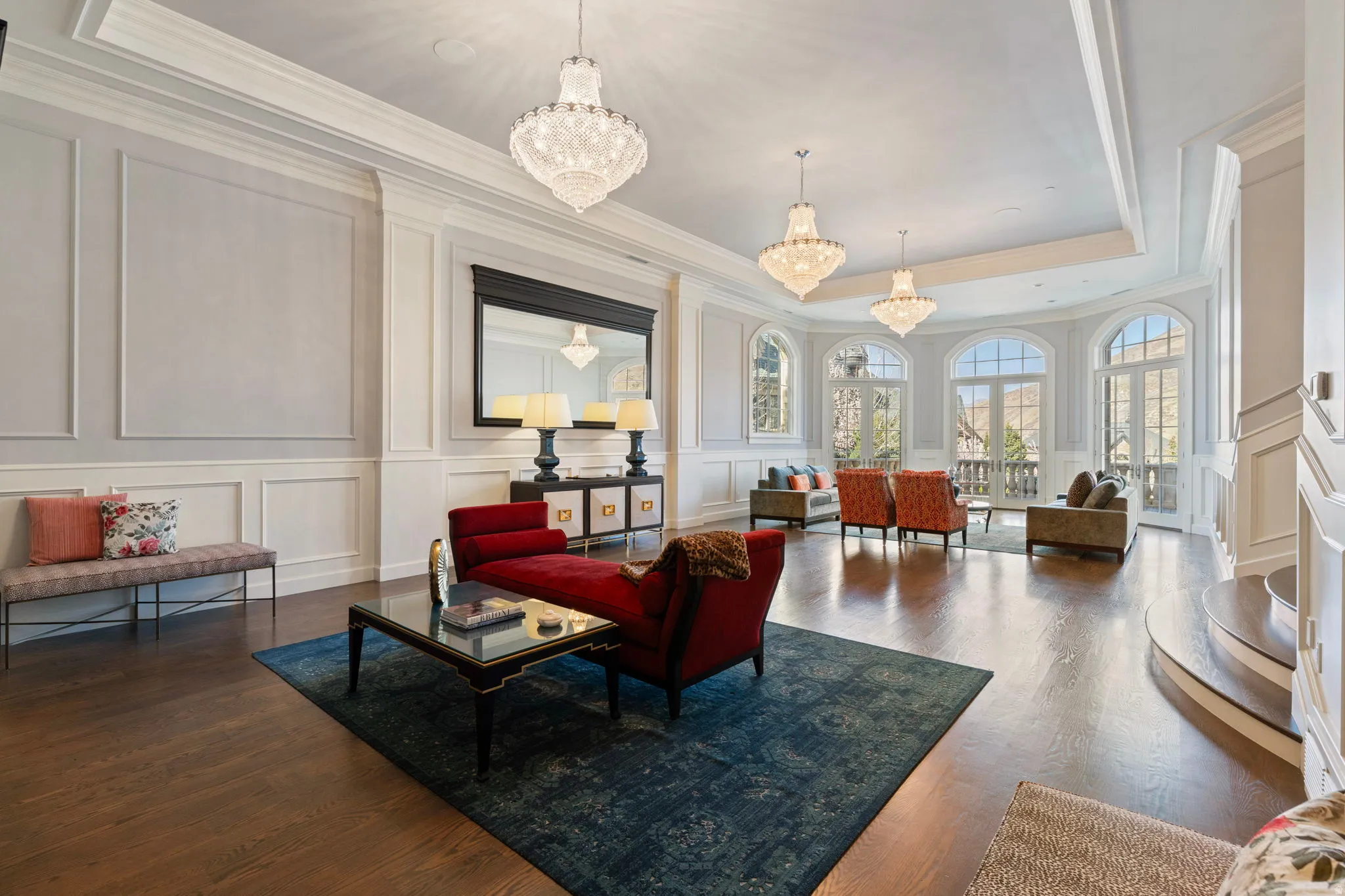 Living area featuring a decorative wall, a tray ceiling, suspended lighting, dark wood-style floors, and ornamental molding