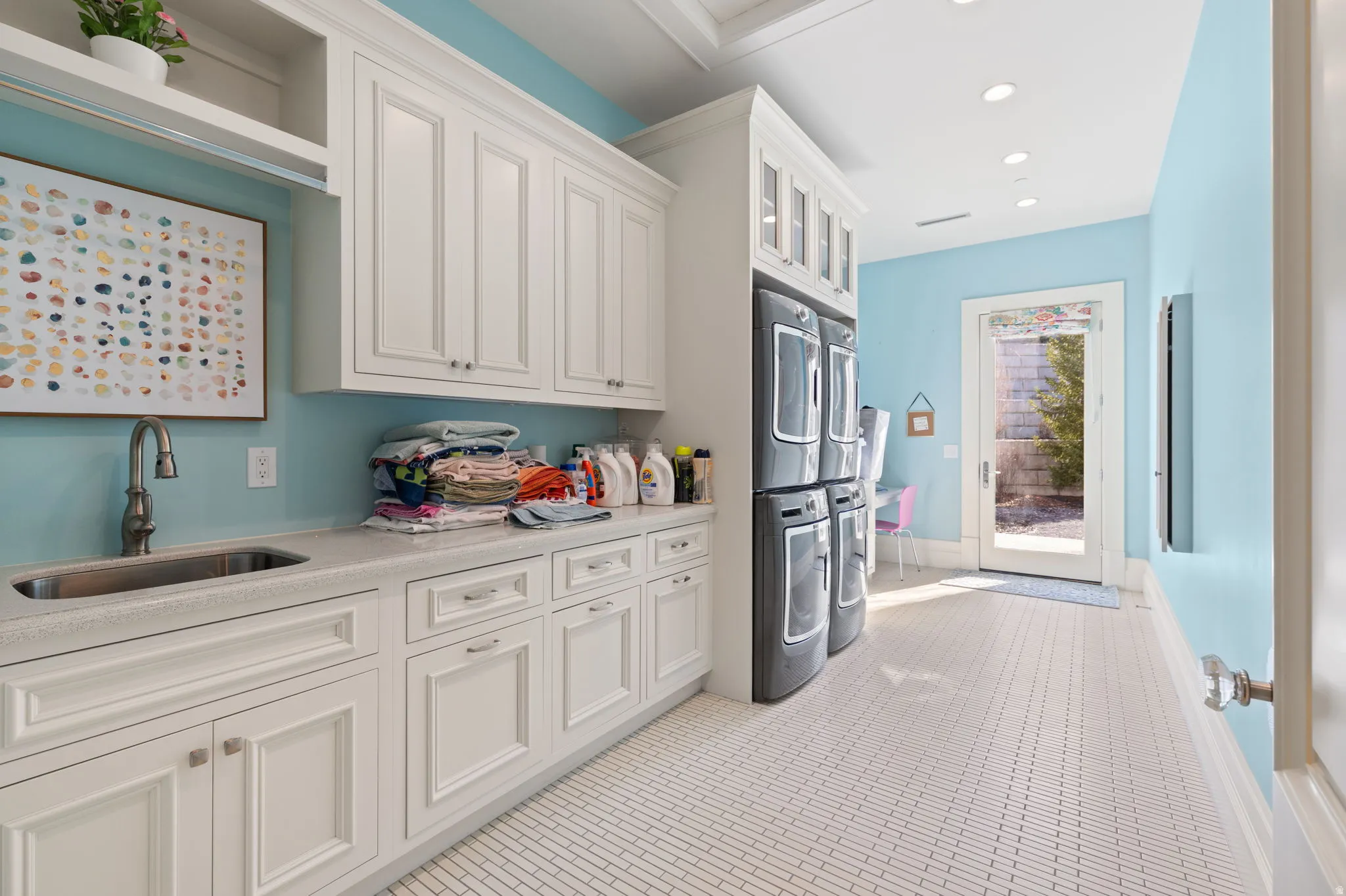 Kitchen featuring stacked washer / dryer, white cabinets, glass insert cabinets, light stone counters, and recessed lighting