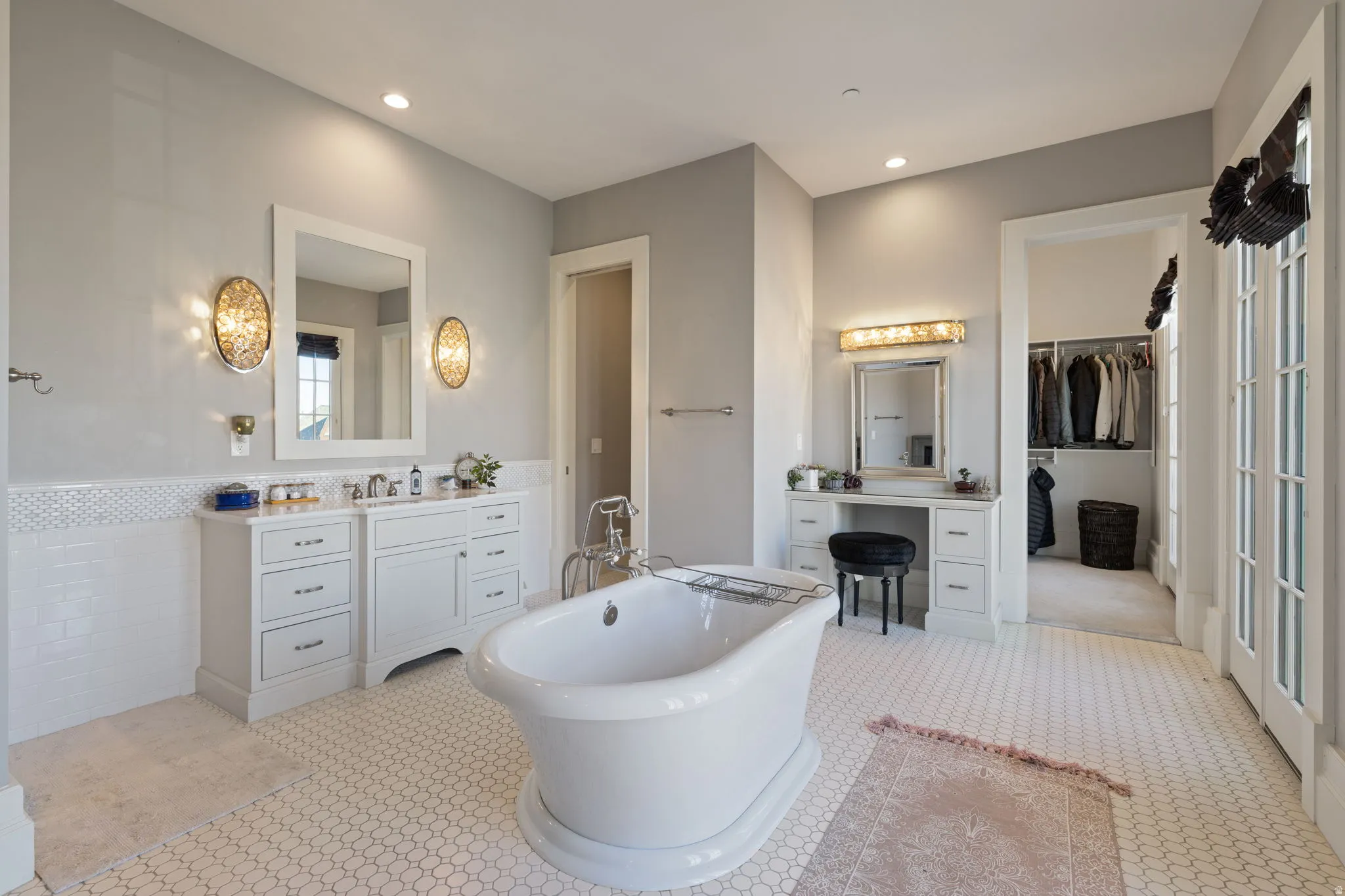 Full bathroom featuring a spacious closet, two vanities, a freestanding tub, recessed lighting, and wainscoting