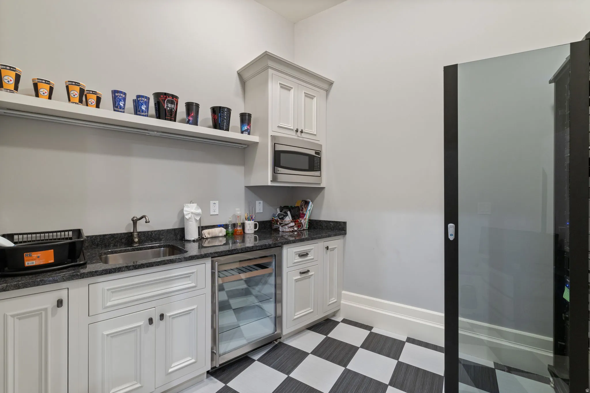 Kitchen with dark floors, wine cooler, dark stone countertops, white cabinetry, and stainless steel microwave