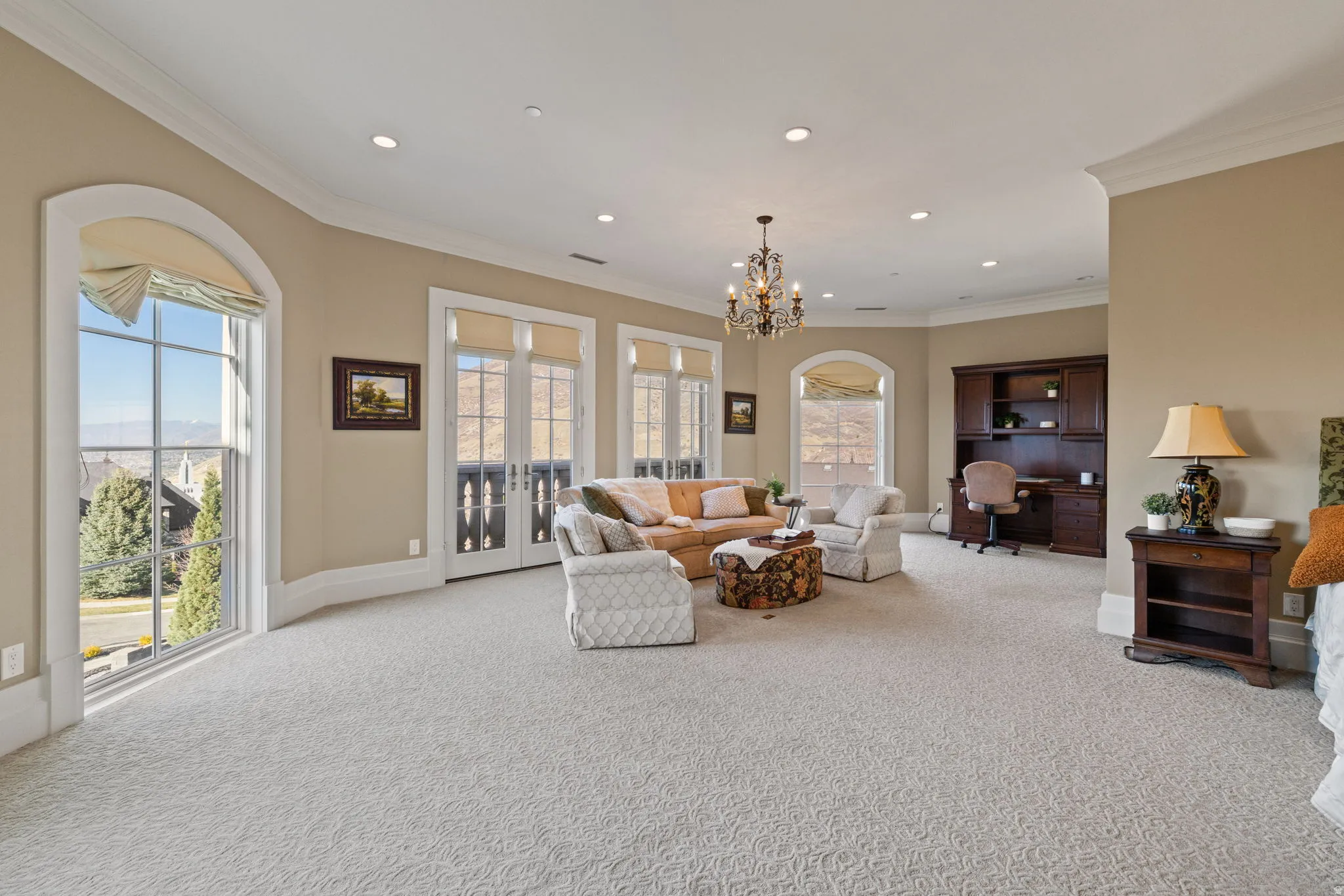 Living area featuring light carpet, crown molding, a chandelier, arched walkways, and an office area