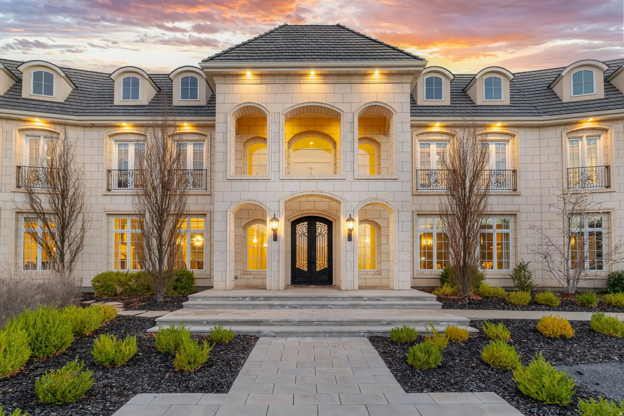Back of house at dusk with stone siding and a balcony