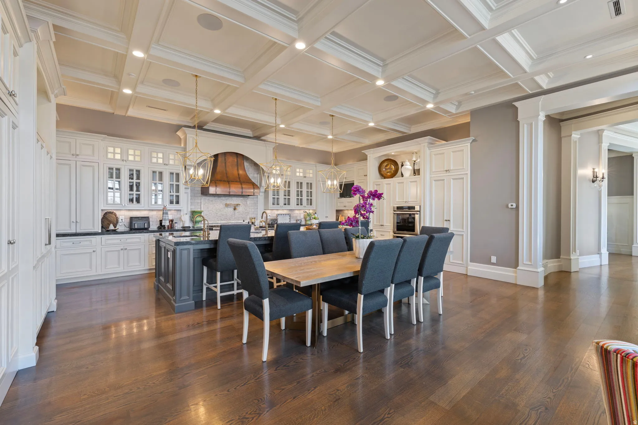 Dining area featuring ornate columns, dark wood finished floors, a chandelier, coffered ceiling, and crown molding