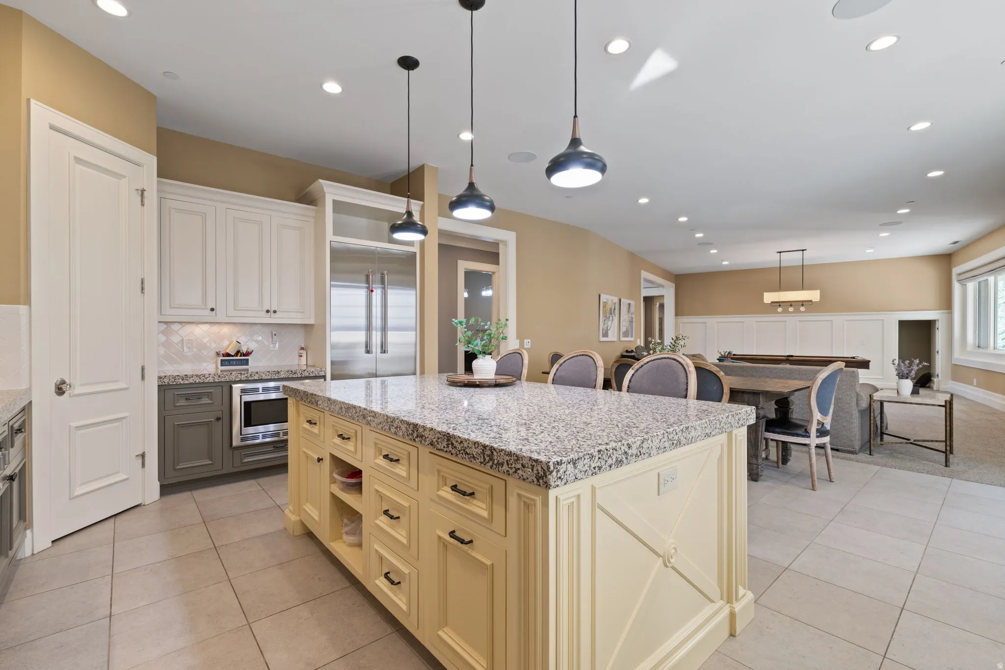 Kitchen featuring decorative light fixtures, light stone counters, a kitchen island, built in fridge, and backsplash