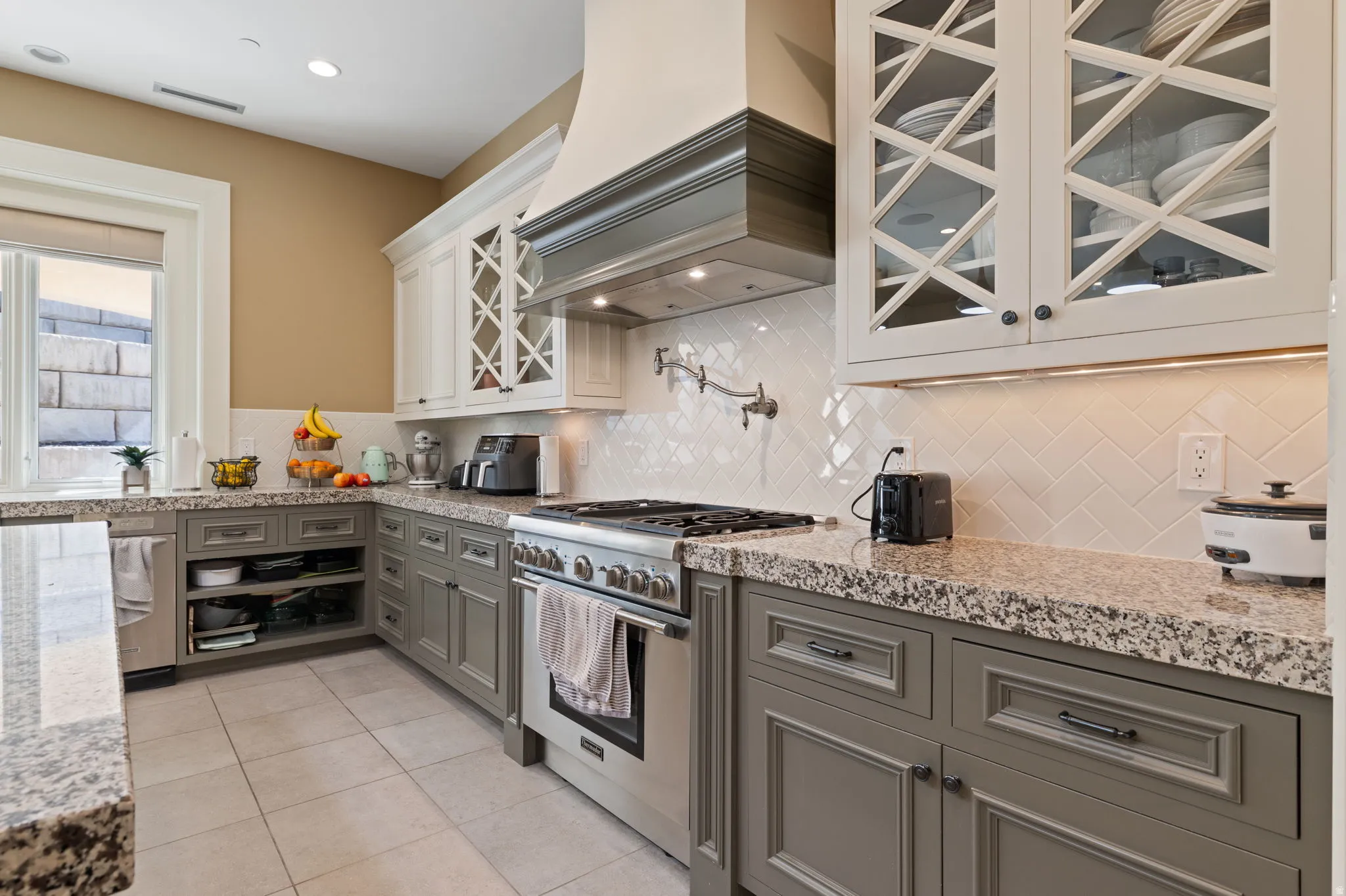 Dual tone kitchen featuring high end stove, glass insert cabinets, light stone counters, dual tone cabinetry, and light tile patterned floors